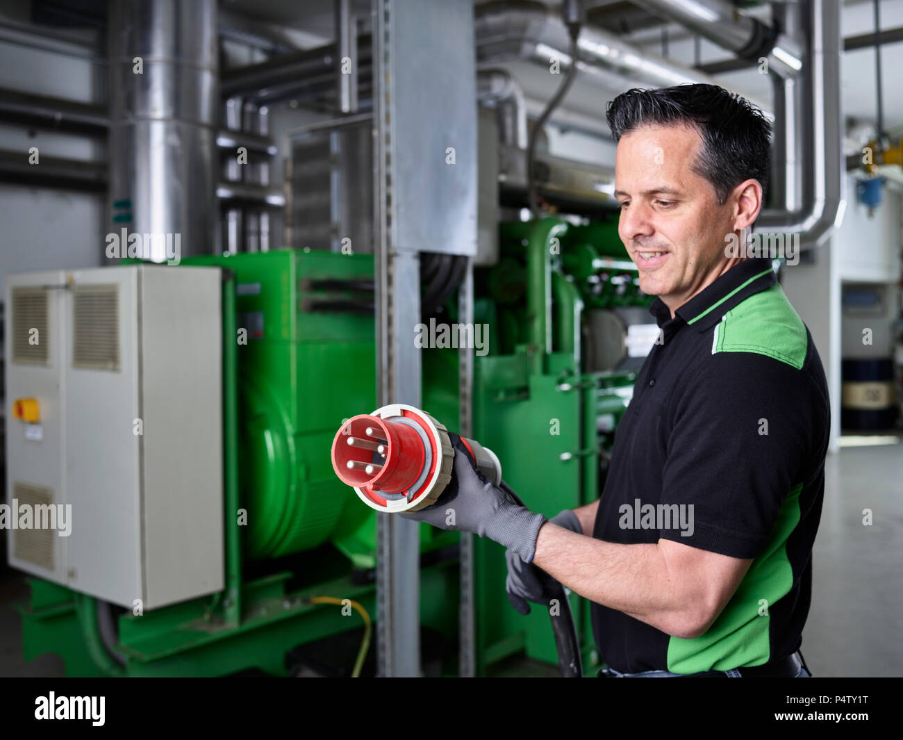 Impianto di cogenerazione di energia termica ed elettrica, lavoratore tenendo alta la spina di corrente Foto Stock