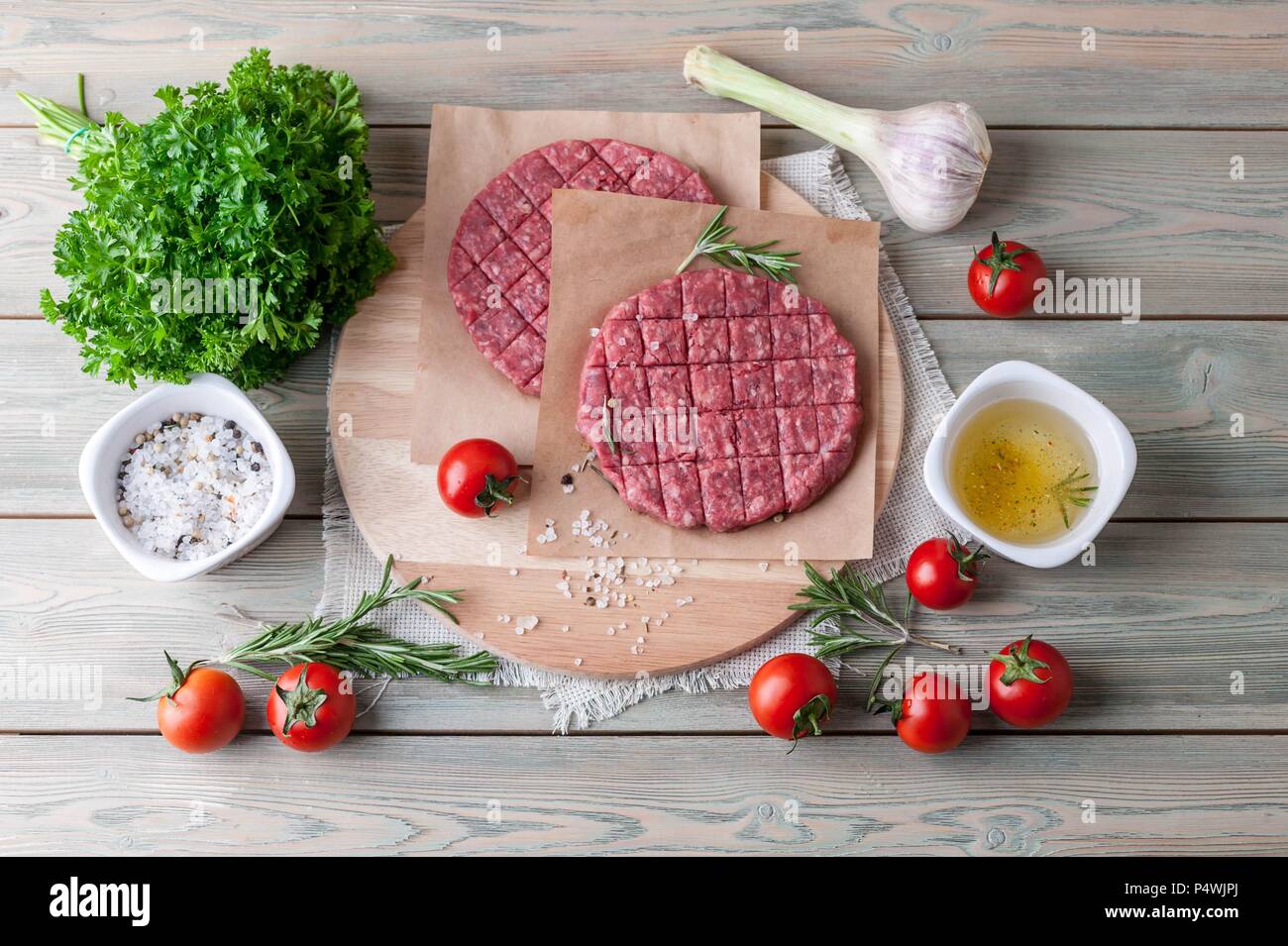 Materie hamburger cotoletta su una tavola di legno con le spezie e le erbe aromatiche e i pomodori ciliegia. Vista superiore Foto Stock