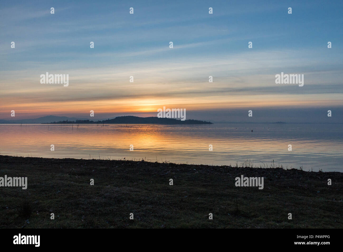 Una ripresa di un tramonto su un lago, con molte linee diagonali creato dalle nuvole e la costa Foto Stock