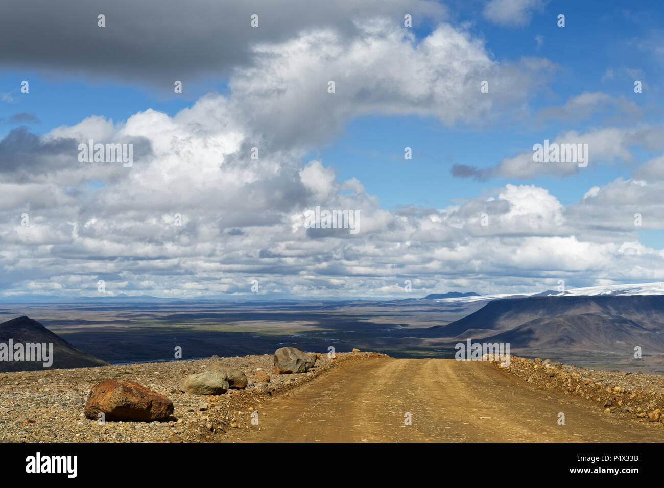 Una strada sterrata che conduce su una piccola collina, dietro di esso è un ampio paesaggio di pianura, catene montuose e ghiacciai per vedere, al di sopra del cielo blu con bianco e gr Foto Stock