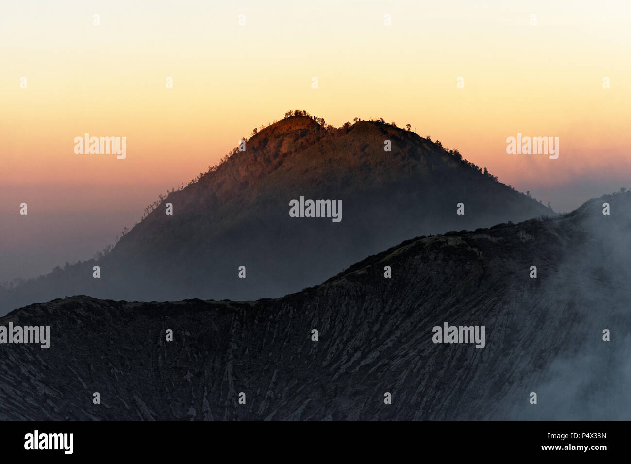 La prima luce del giorno al vulcano attivo Ijen, vista da circa tremila metri di altezza bordo del cratere di un vulcano opposta cratere, il cielo in sfumature di Foto Stock