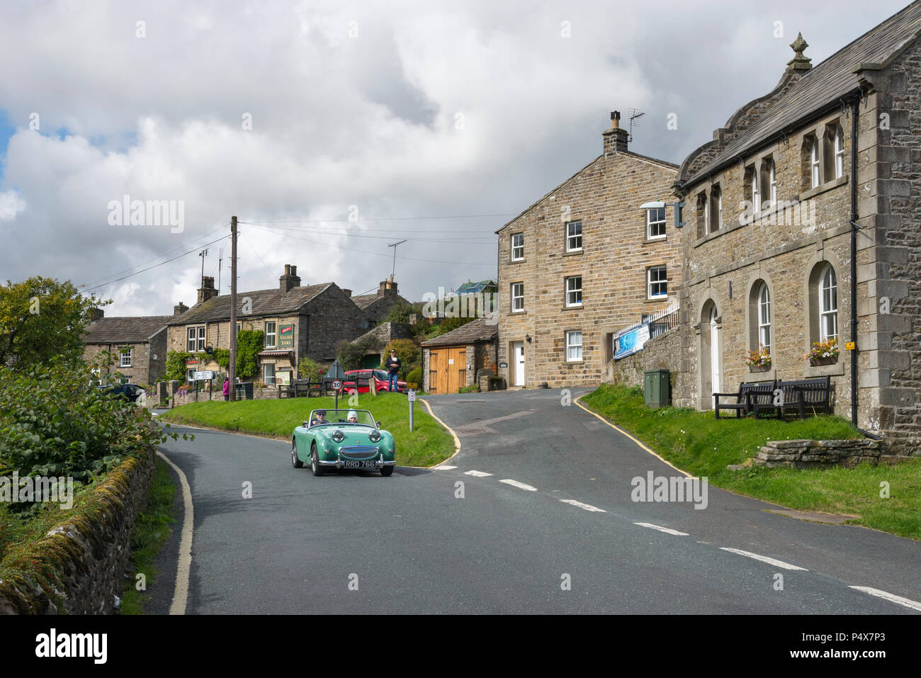 Giovane alla guida di un'auto d'epoca attraverso il villaggio di Muker in Swaledale, Yorkshire Dales, Inghilterra. Foto Stock