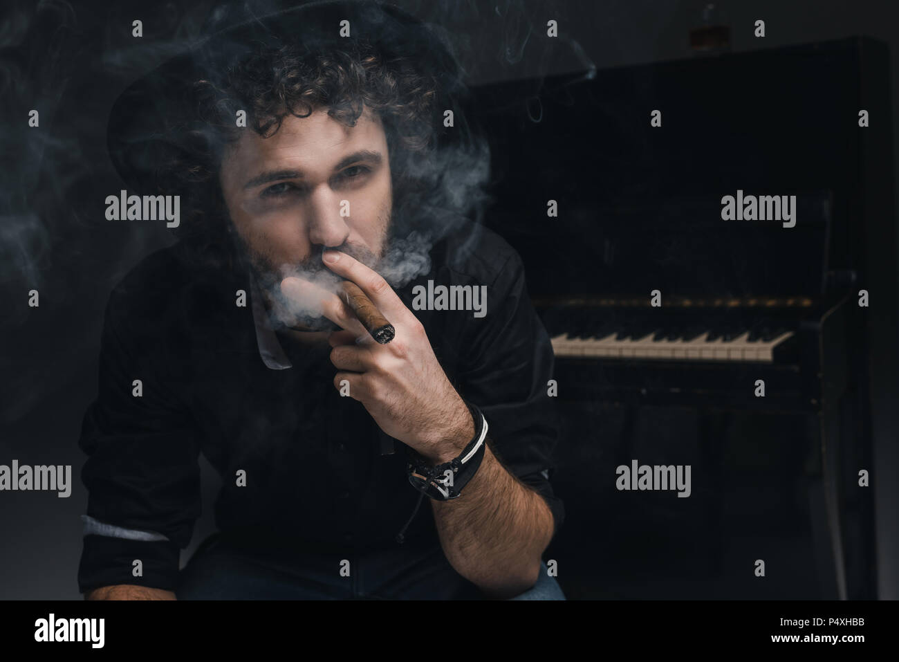 Bello il musicista di fumare il sigaro nella parte anteriore del piano su nero Foto Stock