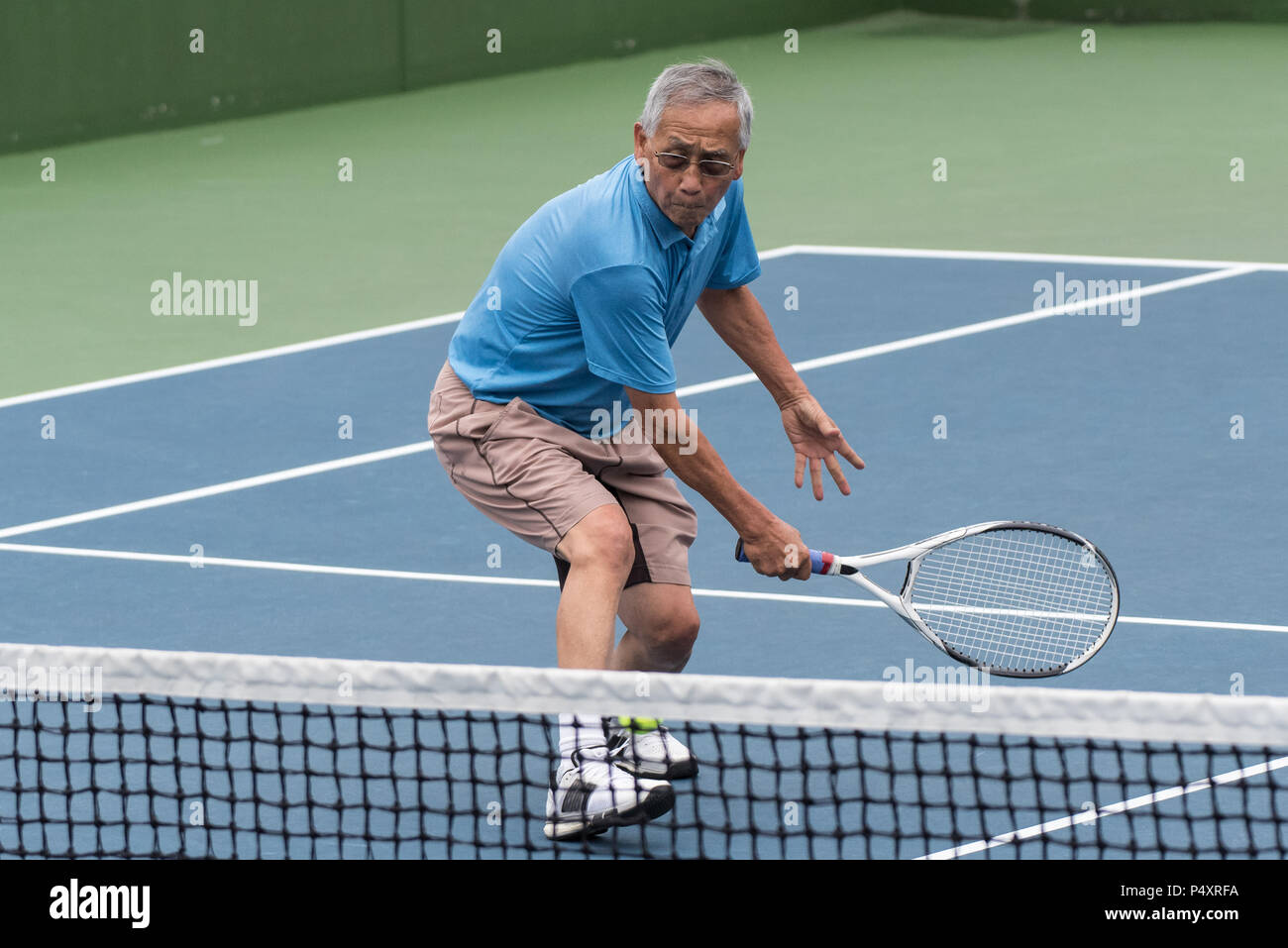 Healthy Chinese uomo anziano che mostra la flessibilità mentre per raggiungere il basso scritto da tennis volley. Foto Stock