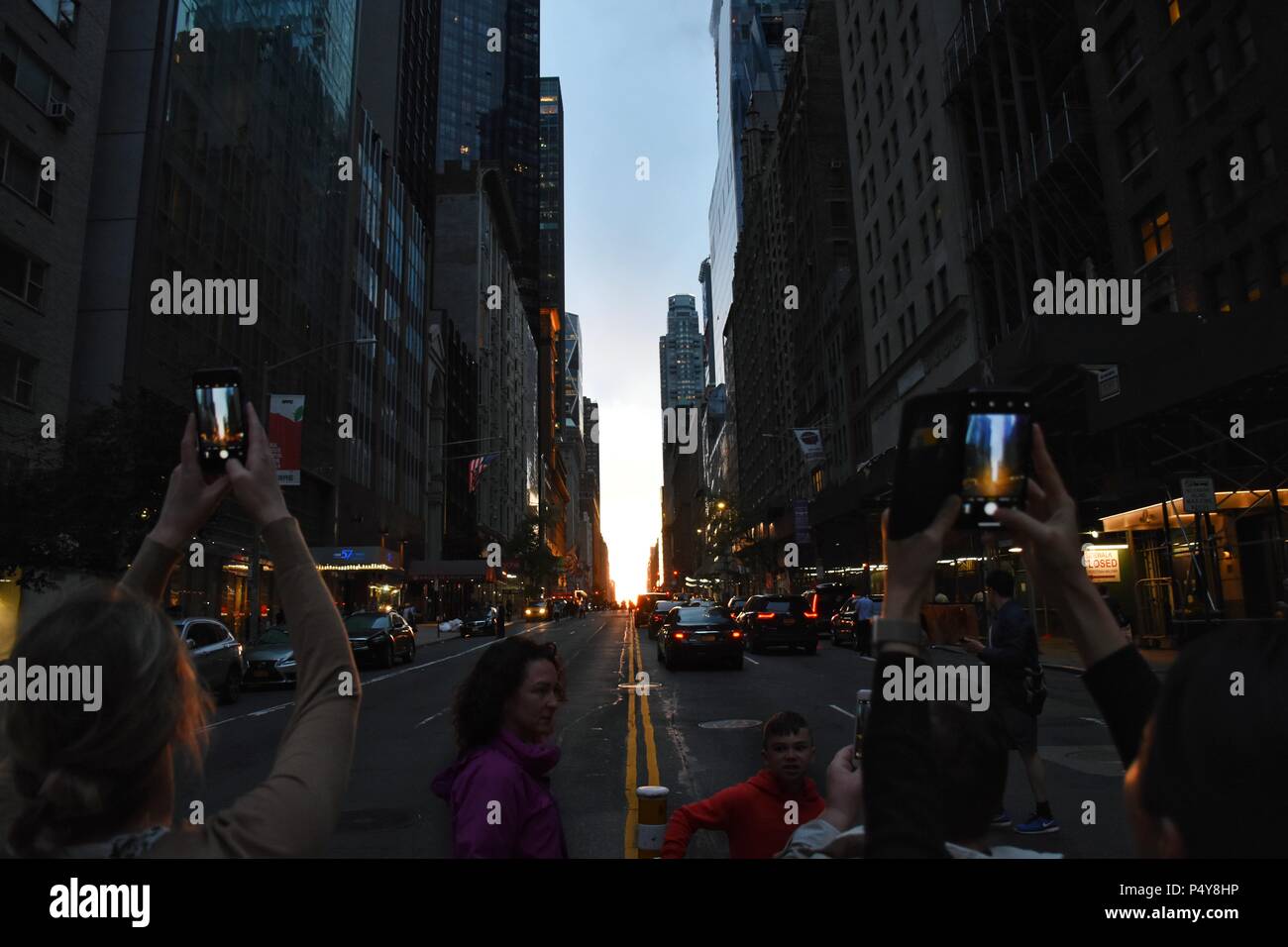 Le fotocamere dello smartphone per raggiungere il cielo per catturare la speciale 'Manhattanhenge' tramonto in New York City (quando il tramonto si allinea con le strade) Foto Stock