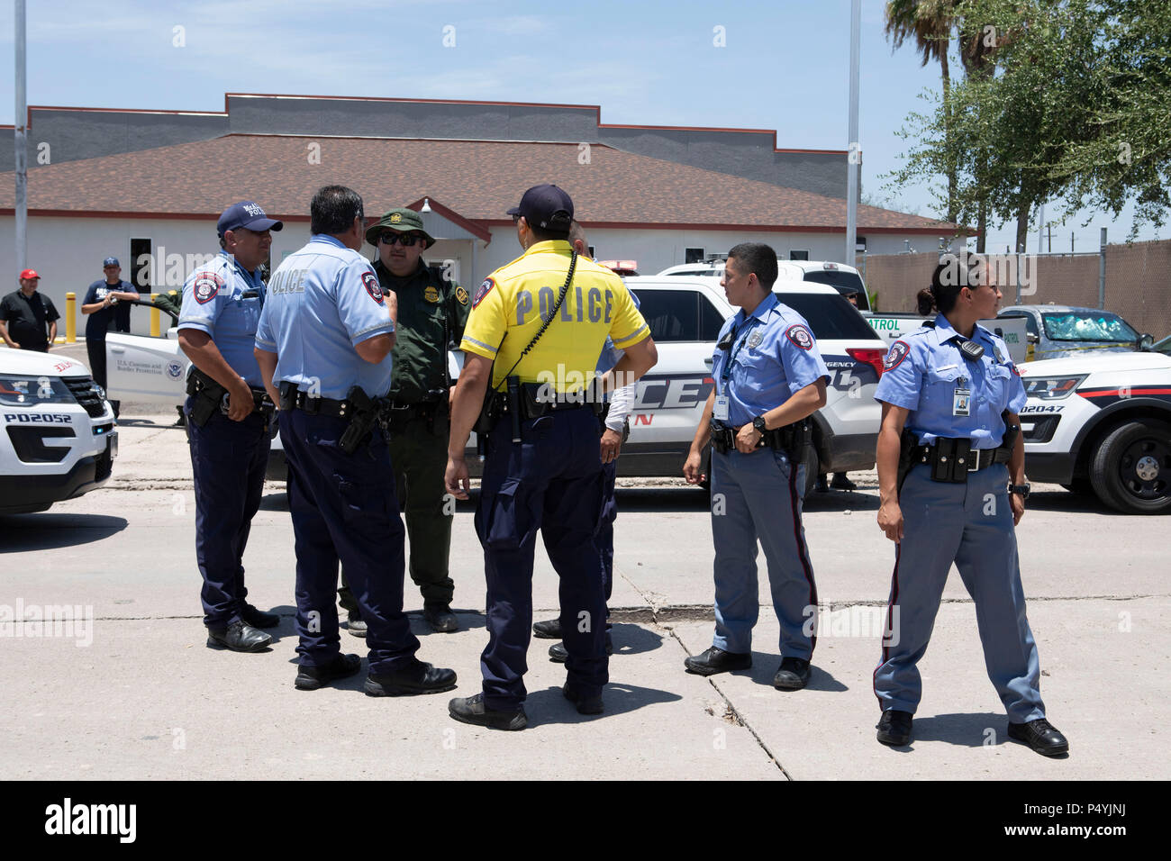 Stati Uniti Pattuglia di Confine e McAllen Guardia di polizia un immigrato centro di detenzione mentre i manifestanti blocco un governo bus con figli di immigrati a bordo per tenerlo da lasciare. Foto Stock