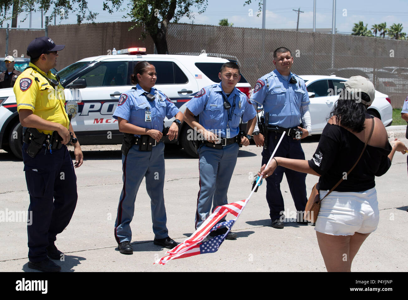 Stati Uniti Pattuglia di Confine e McAllen Guardia di polizia un immigrato centro di detenzione mentre i manifestanti blocco un governo bus con figli di immigrati a bordo per tenerlo da lasciare. Foto Stock