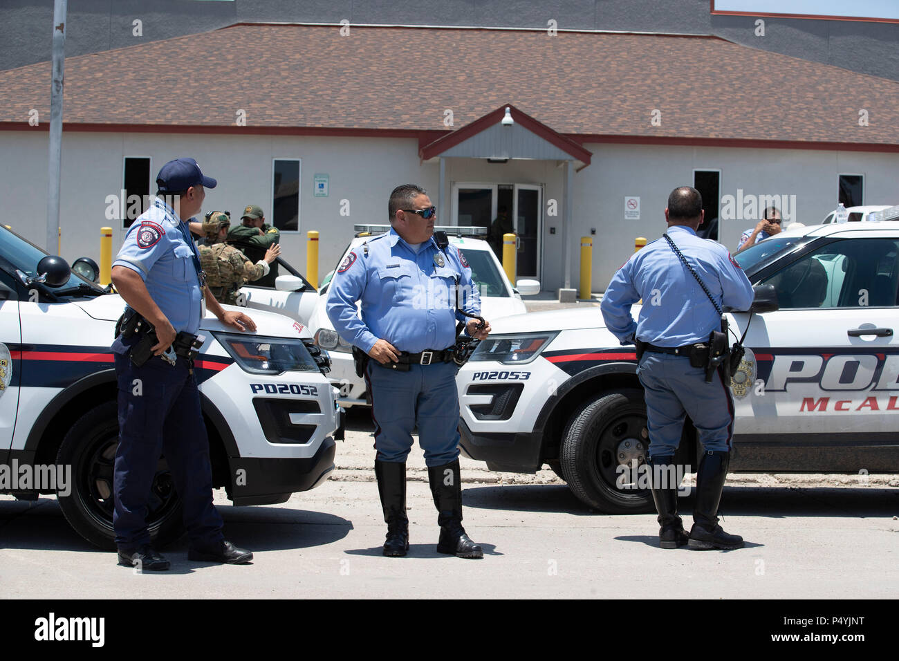 Stati Uniti Pattuglia di Confine e McAllen Guardia di polizia un immigrato centro di detenzione mentre i manifestanti blocco un governo bus con figli di immigrati a bordo per tenerlo da lasciare. Foto Stock