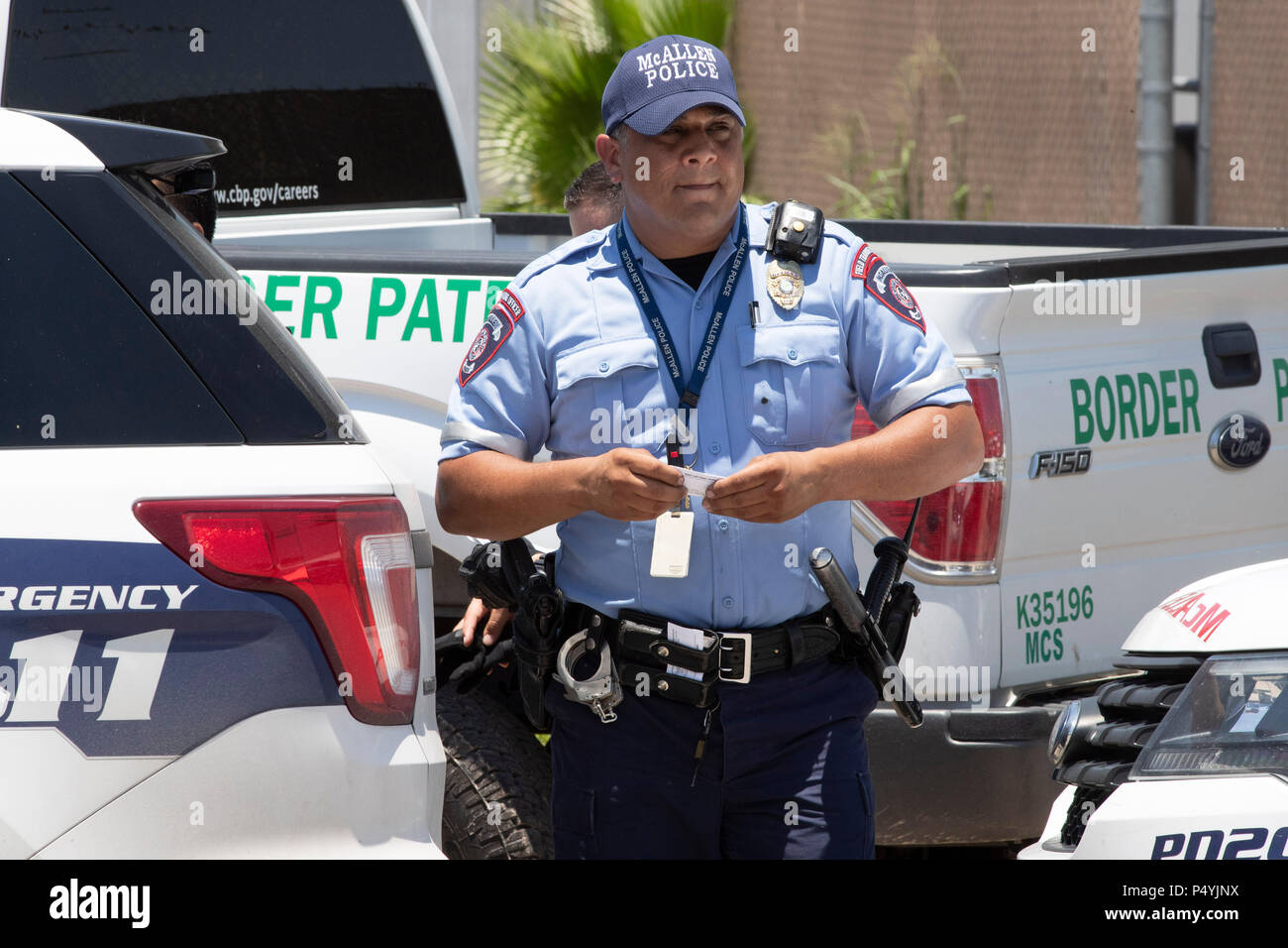 Stati Uniti Pattuglia di Confine e McAllen Guardia di polizia un immigrato centro di detenzione mentre i manifestanti blocco un governo bus con figli di immigrati a bordo per tenerlo da lasciare. Foto Stock