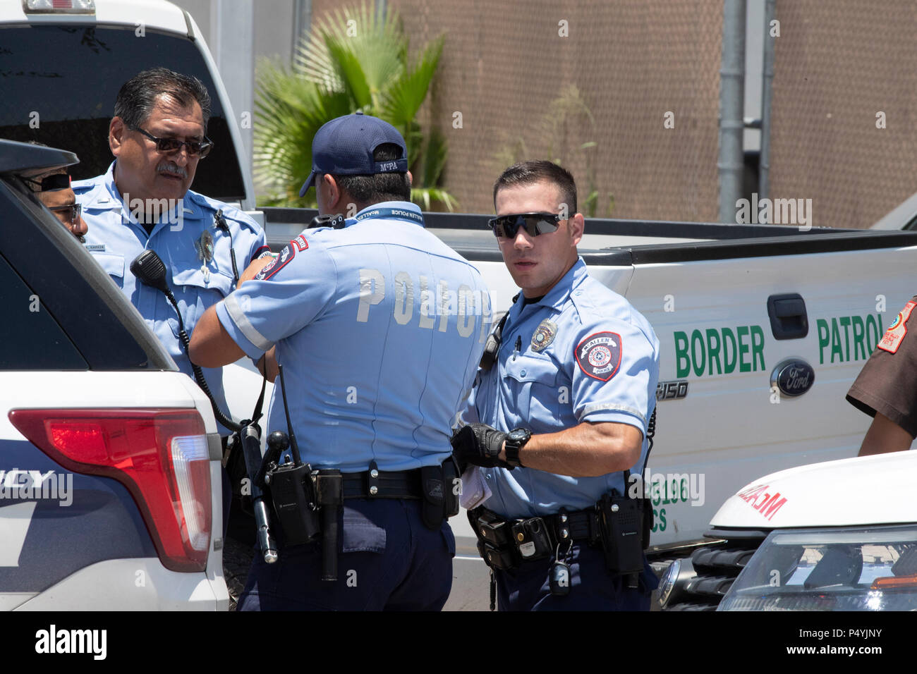 Stati Uniti Pattuglia di Confine e McAllen Guardia di polizia un immigrato centro di detenzione mentre i manifestanti blocco un governo bus con figli di immigrati a bordo per tenerlo da lasciare. Foto Stock