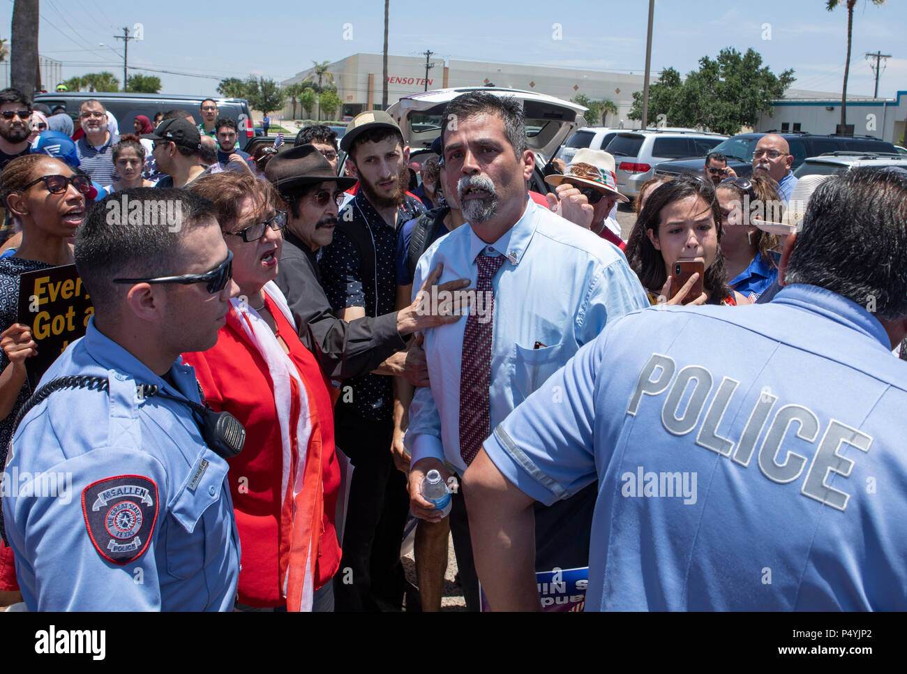 Stati Uniti Pattuglia di Confine e McAllen Guardia di polizia un immigrato centro di detenzione mentre i manifestanti blocco un governo bus con figli di immigrati a bordo per tenerlo da lasciare. Foto Stock