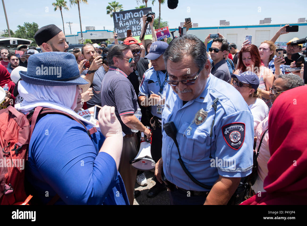 Stati Uniti Pattuglia di Confine e McAllen Guardia di polizia un immigrato centro di detenzione mentre i manifestanti blocco un governo bus con figli di immigrati a bordo per tenerlo da lasciare. Foto Stock