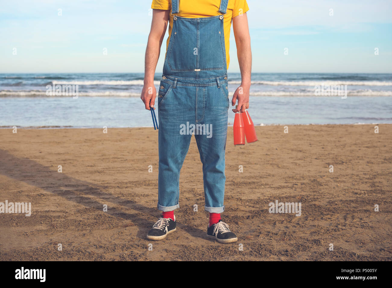 Uomo in salopette da permanente sulla spiaggia tenendo le bottiglie di bevande analcoliche Foto Stock