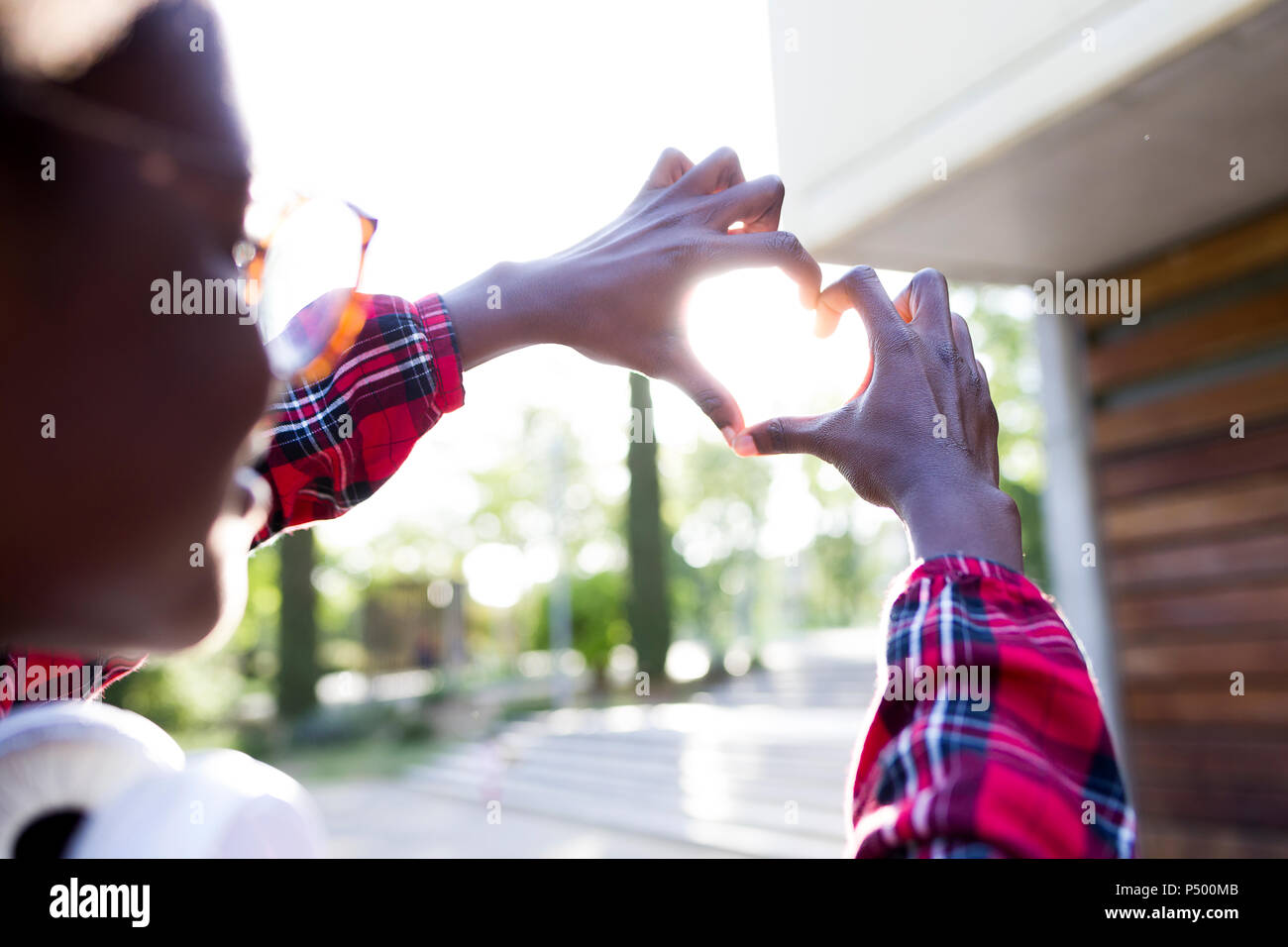 Giovane donna mani di sagomatura di un cuore contro la luce solare Foto Stock