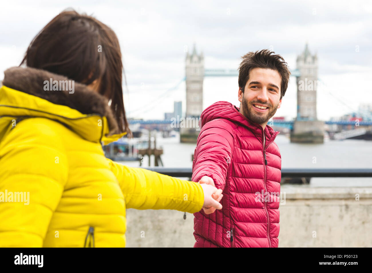 UK, Londra, Ritratto di giovane sorridente man standing mano nella mano sul ponte sul Tamigi con la sua ragazza Foto Stock