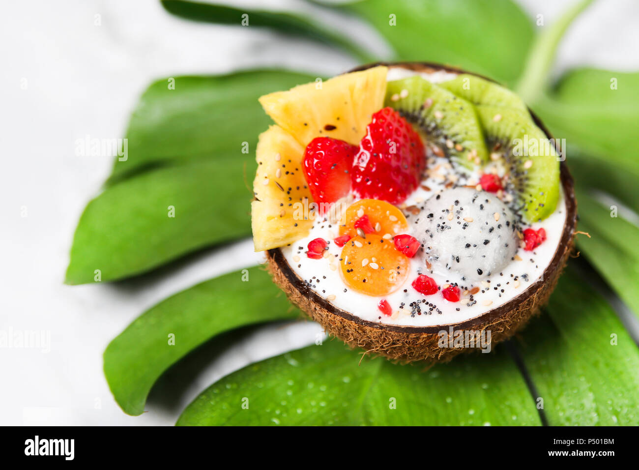 Ciotola di noce di cocco con vario frutta, yogurt naturale e semi sulla foglia Foto Stock