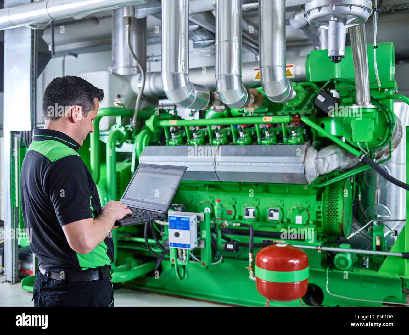Impianto di cogenerazione di energia termica ed elettrica, lavoratore utilizzando laptop nella parte anteriore del motore a gas Foto Stock