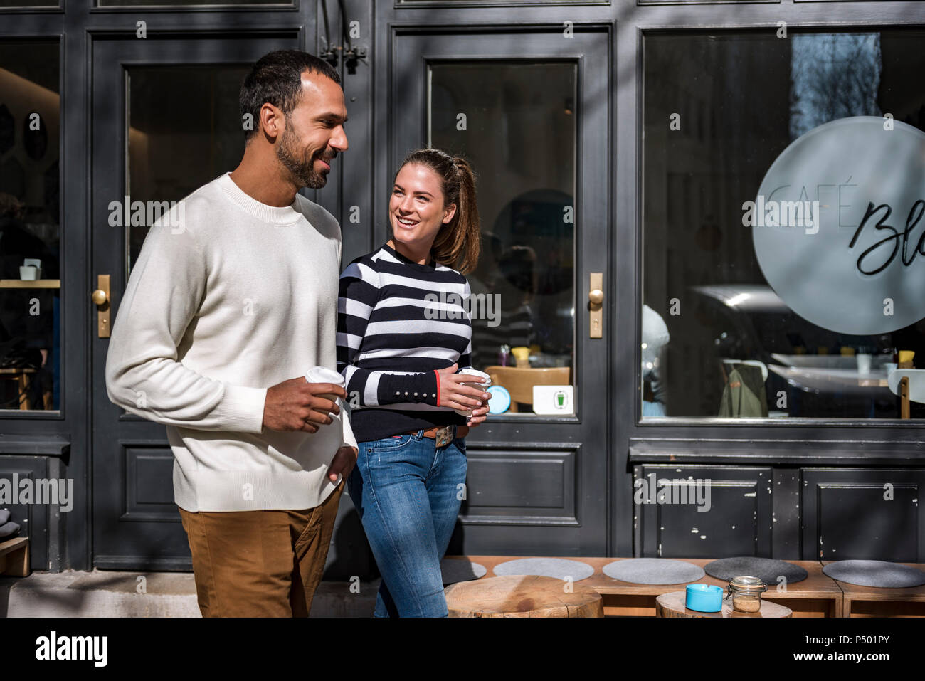 Uomo e donna con coppe da asporto a piedi al di fuori di un cafe Foto Stock
