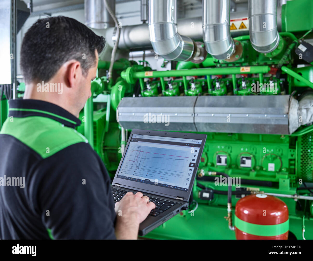 Impianto di cogenerazione di energia termica ed elettrica, lavoratore utilizzando laptop nella parte anteriore del motore a gas Foto Stock