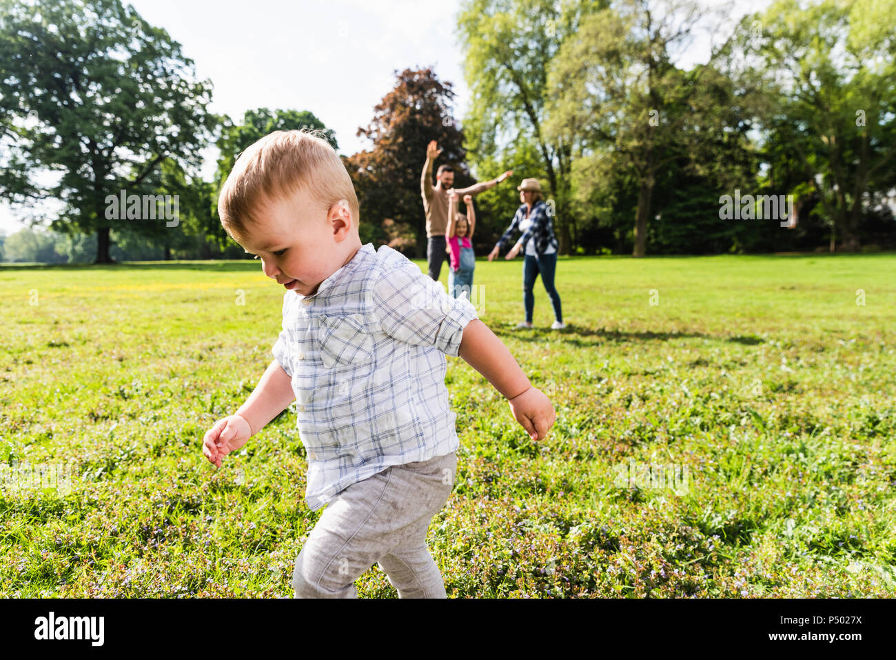 Ragazzo camminando in un parco con la famiglia in background Foto Stock