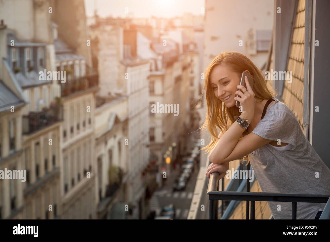 Francia, Parigi, ritratto di donna sorridente al telefono in piedi sul balcone la sera Foto Stock