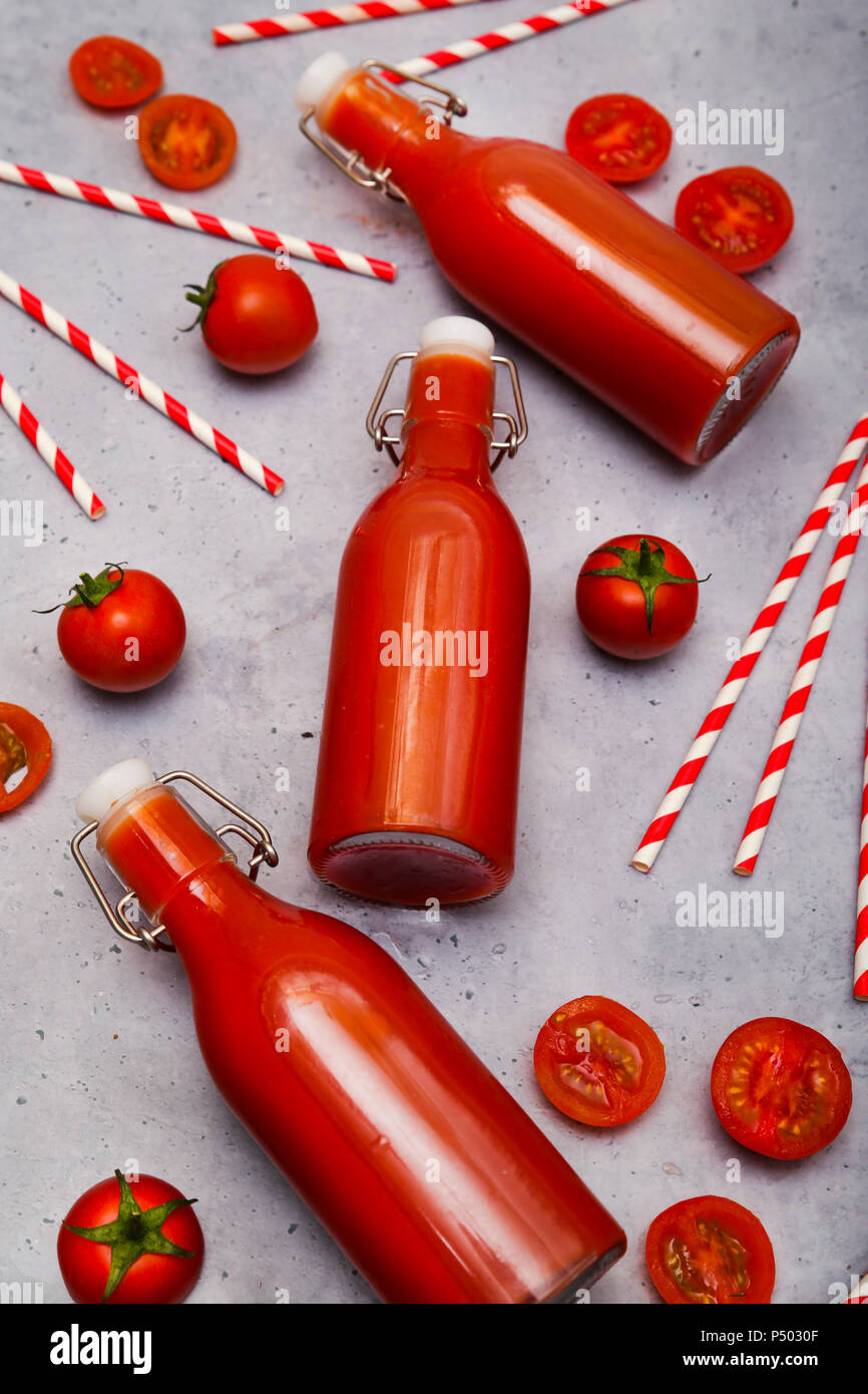 In casa di succo di pomodoro in swing top bottiglie, cannucce e pomodori sul terreno grigio Foto Stock