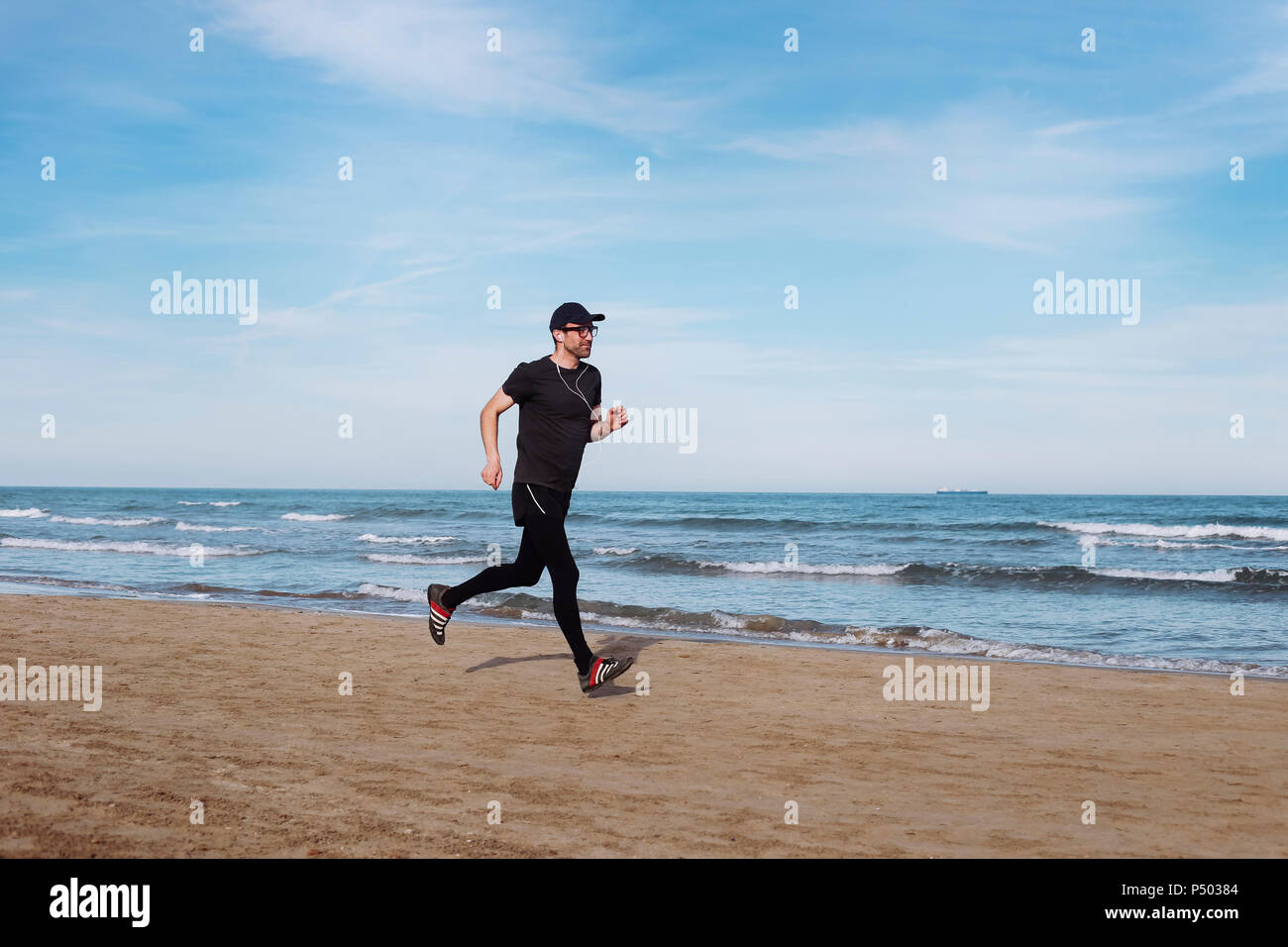 La Spagna, l'uomo vestito di nero jogging sulla spiaggia Foto Stock