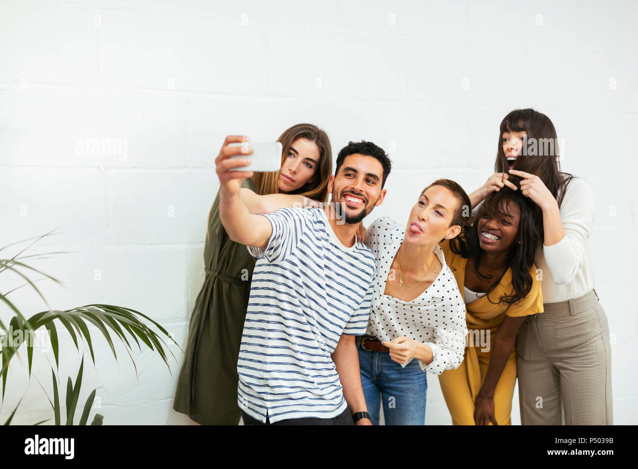 Giocoso i colleghi permanente al muro di mattoni tenendo un selfie Foto Stock