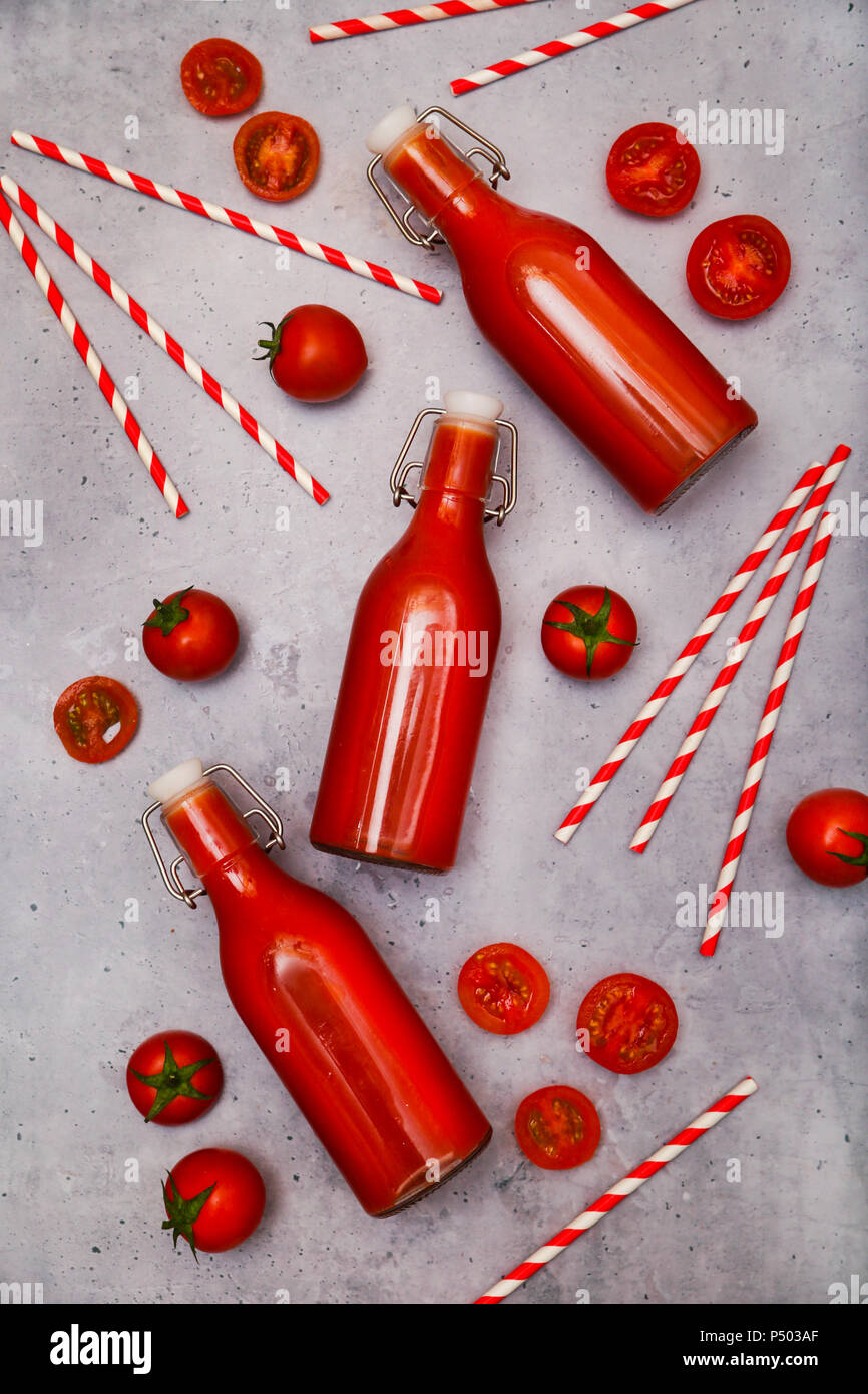 In casa di succo di pomodoro in swing top bottiglie, cannucce e pomodori sul terreno grigio Foto Stock