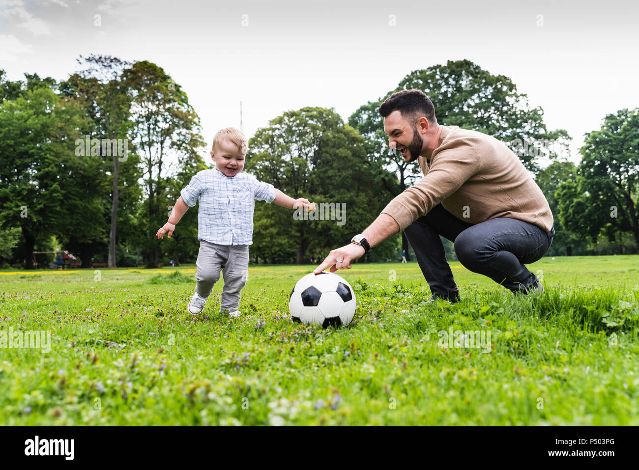 Padre Felice giocando a calcio con il figlio in un parco Foto Stock