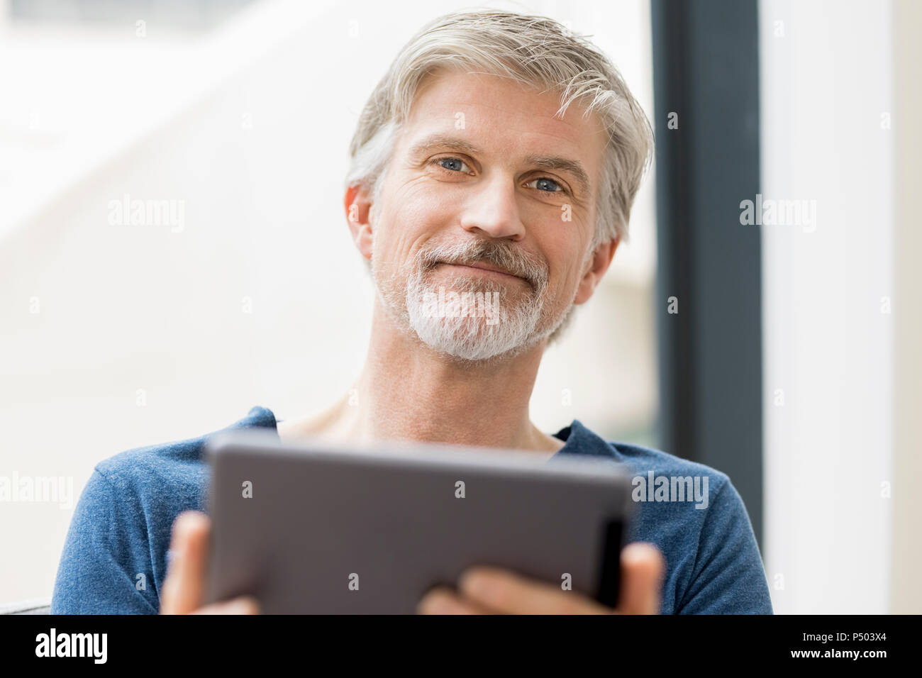 Uomo maturo seduto nel suo ufficio utilizzando la tavoletta digitale Foto Stock