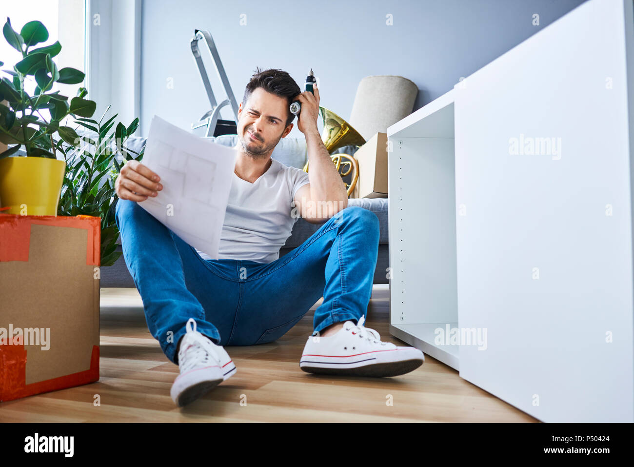 Frustrato uomo lettura mentre le istruzioni di assemblaggio di mobili nel nuovo appartamento Foto Stock