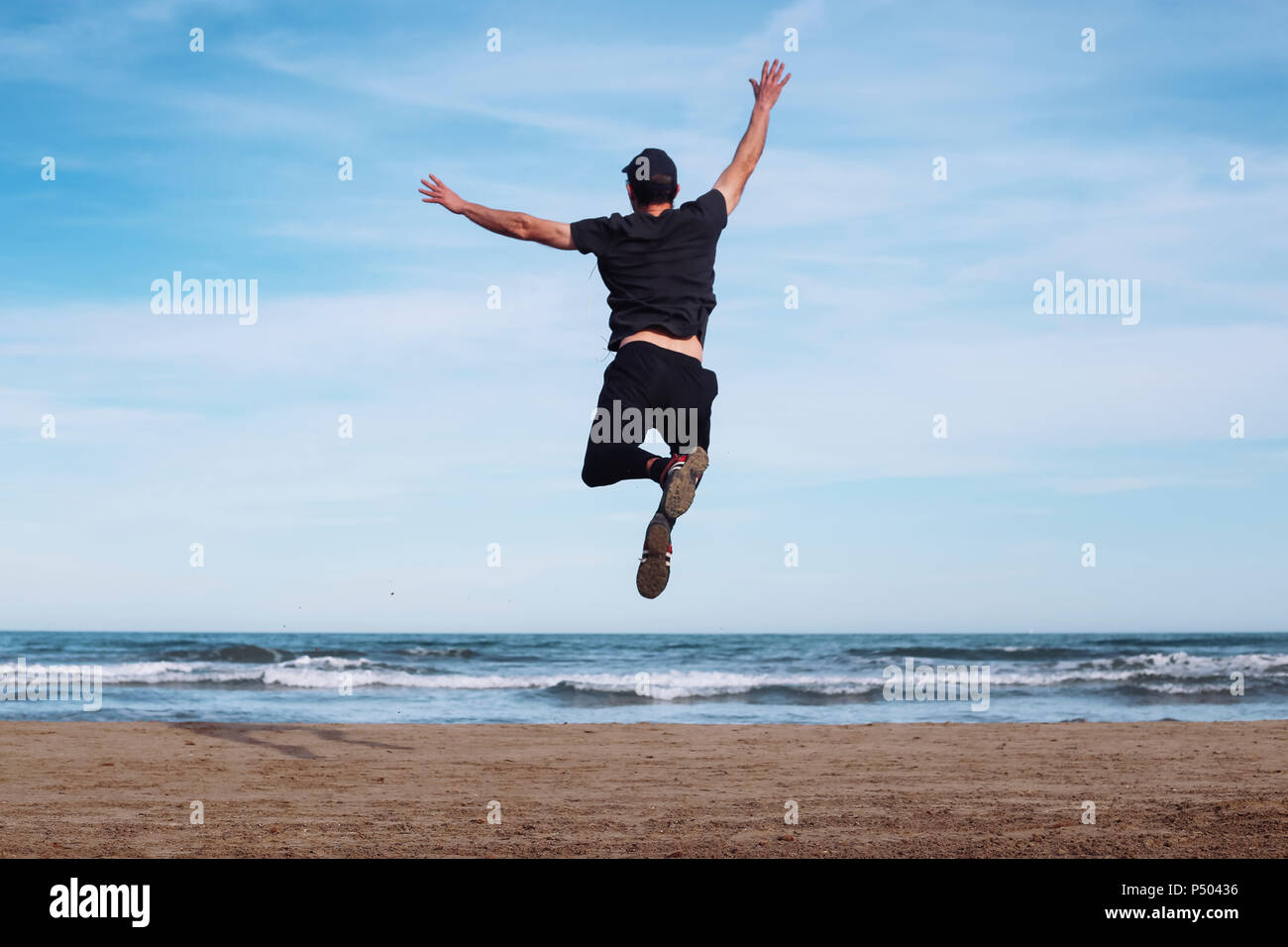 Vista posteriore dell'uomo saltare in aria sulla spiaggia Foto Stock