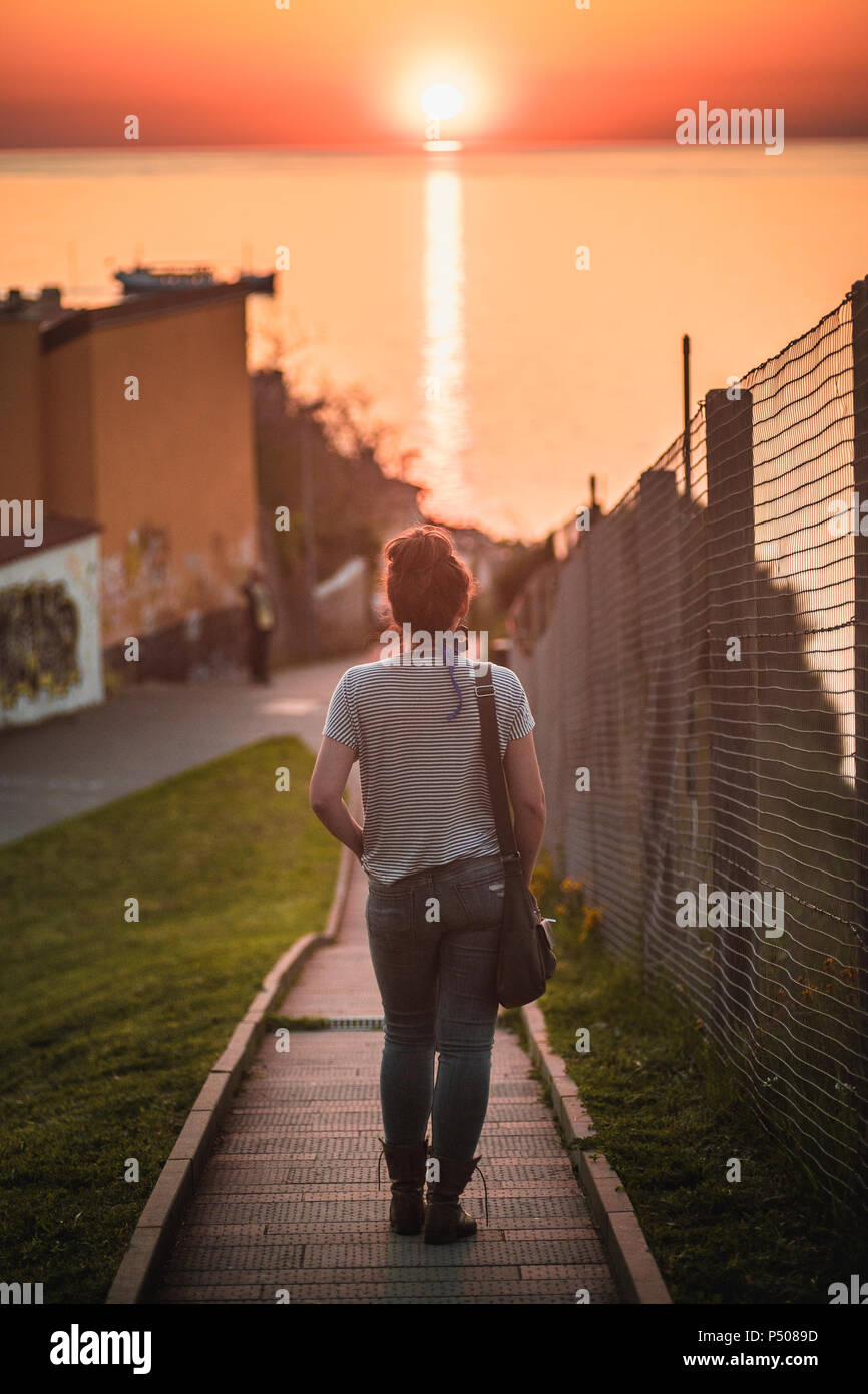 Un giovane viandante cammina verso il tramonto sul mare dopo una giornata di esplorazione. Foto Stock
