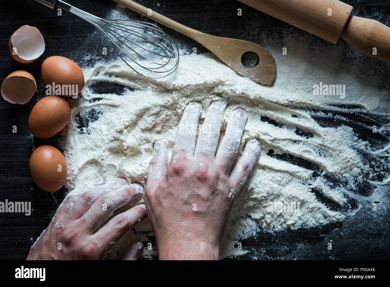 Uomo adulto mani lavorano con la farina. Sfondo con un matterello, farina e uova crude Foto Stock