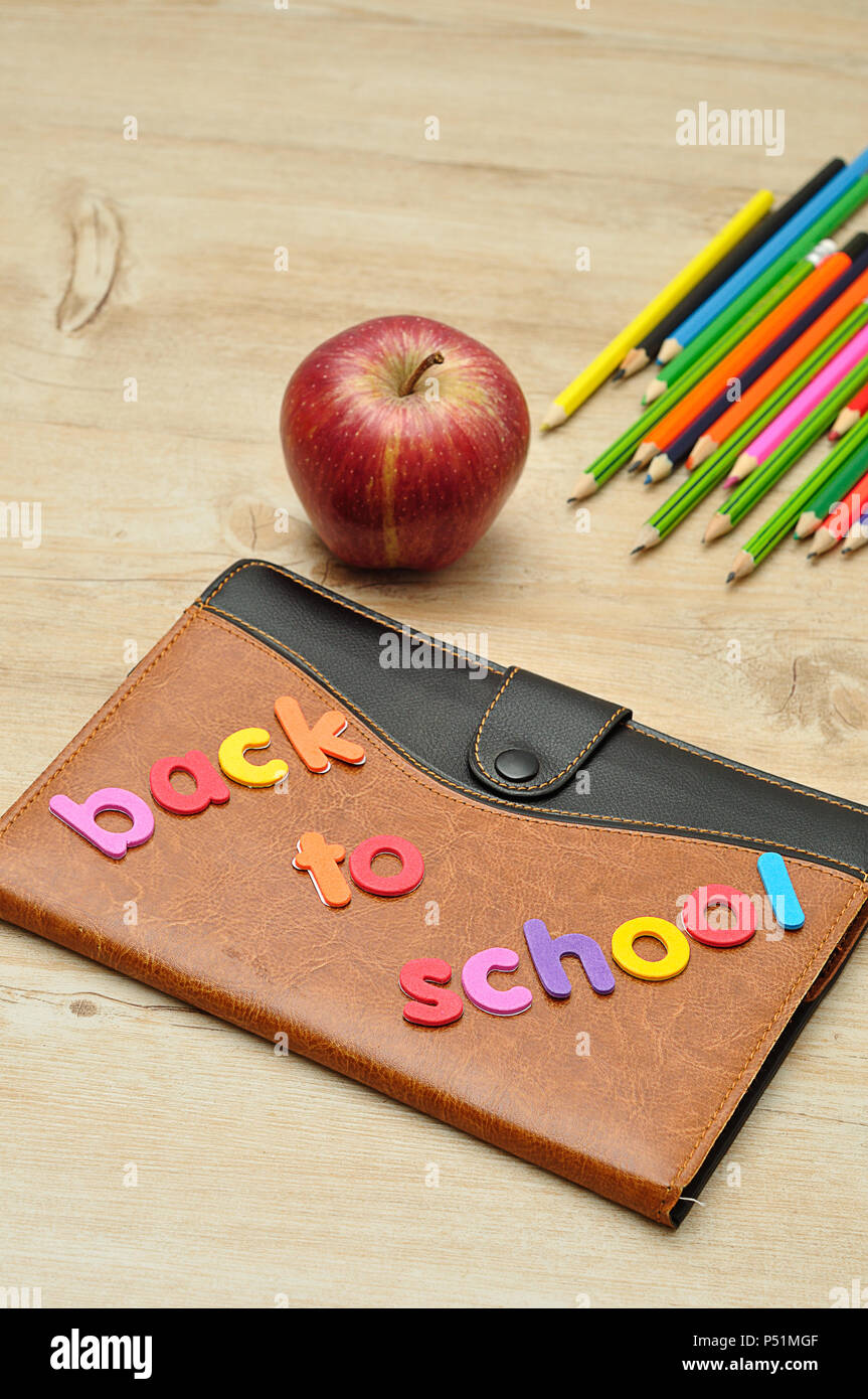 Una coperta di cuoio prenota visualizzata con le parole il ritorno a scuola, un apple e matite colorate Foto Stock