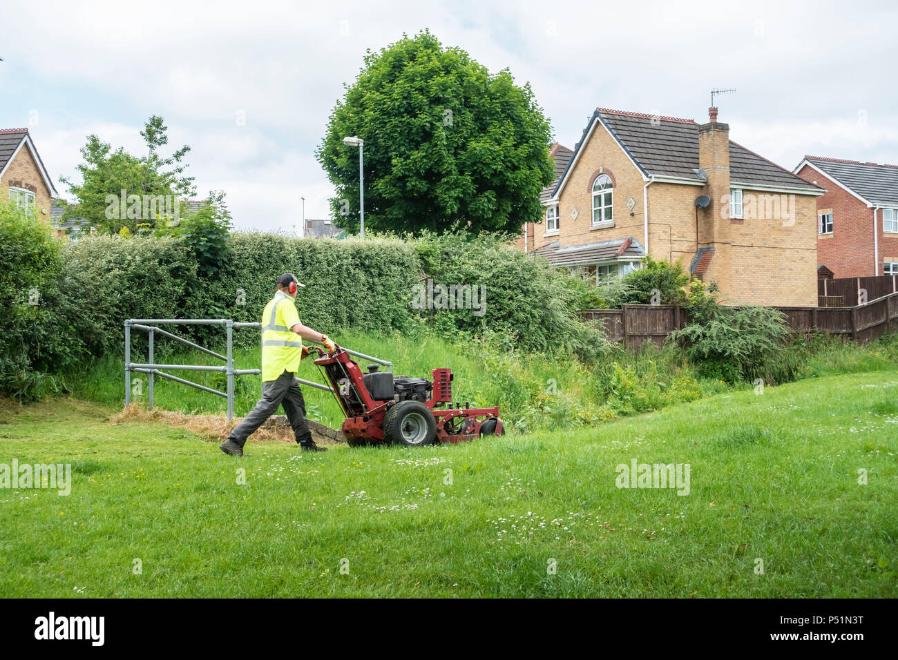 Giardiniere indossando giacca Hi-Vis falciare l'erba su un alloggiamento station wagon. Foto Stock