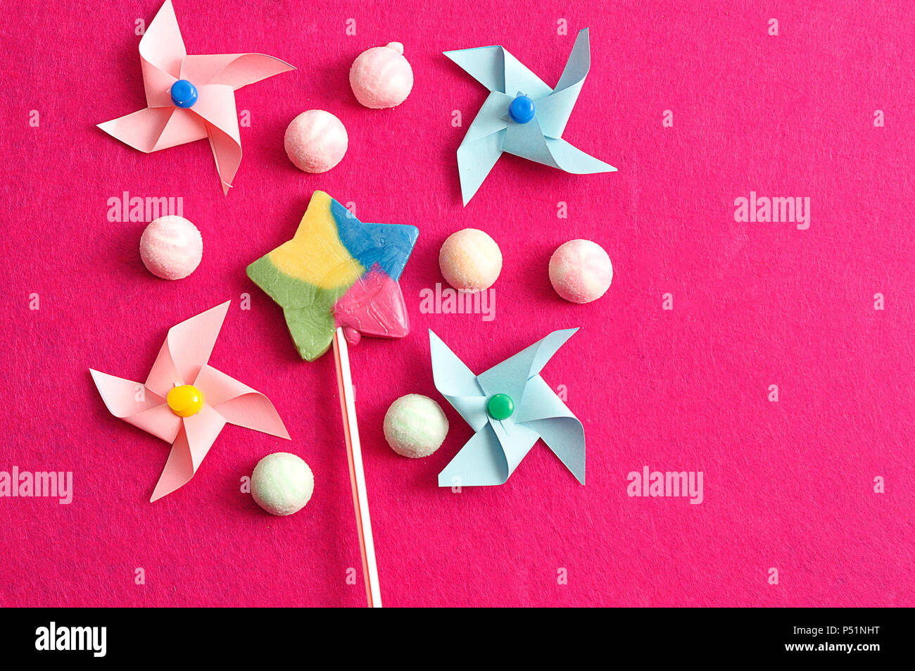 Un colorato forma a stella lollipop visualizzati con colorati pinwheels e marshmallows su uno sfondo rosa Foto Stock