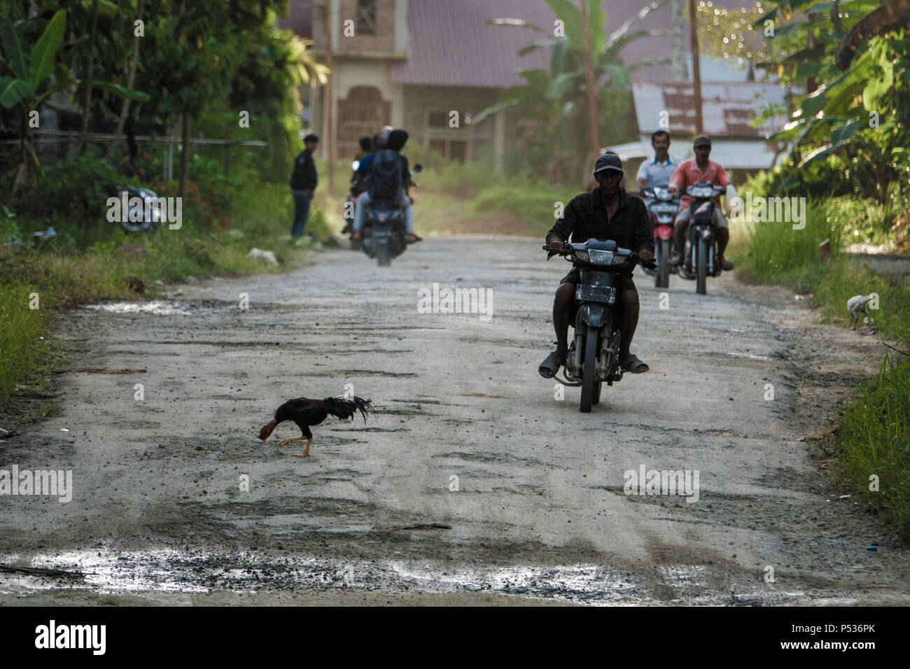 Persone il pendolarismo su uno scooter lungo potholed road in Afulu, isola di Nias, Sumatra, Indonesia Foto Stock