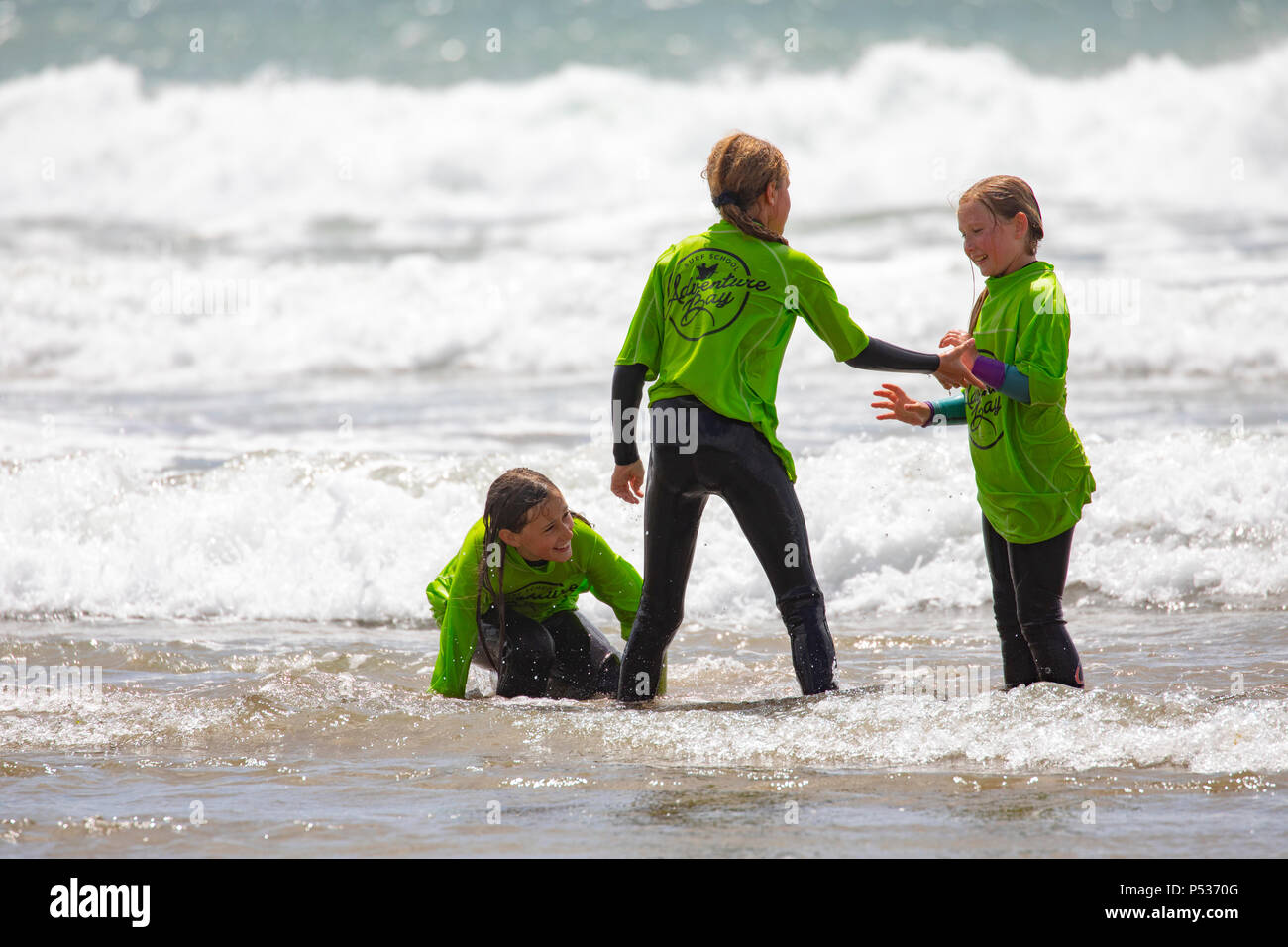 La scuola dei bambini in mute il gioco nel surf prima di una lezione di surf a Whitsand Bay, Cornwall in una calda giornata estiva Foto Stock