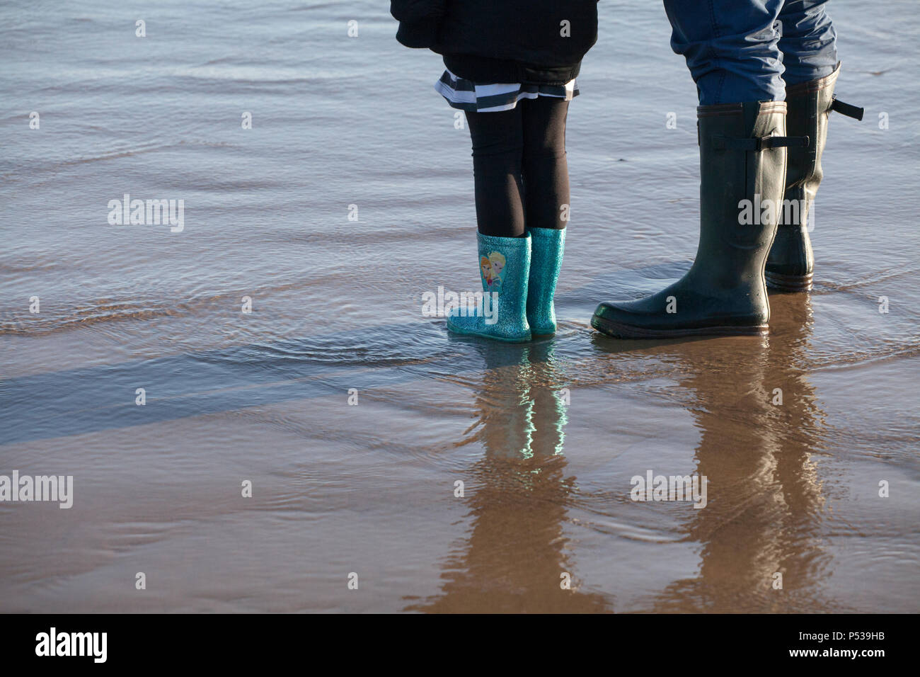 Un uomo e una giovane ragazza stare sulla sabbia bagnata nella loro stivali da pioggia Foto Stock
