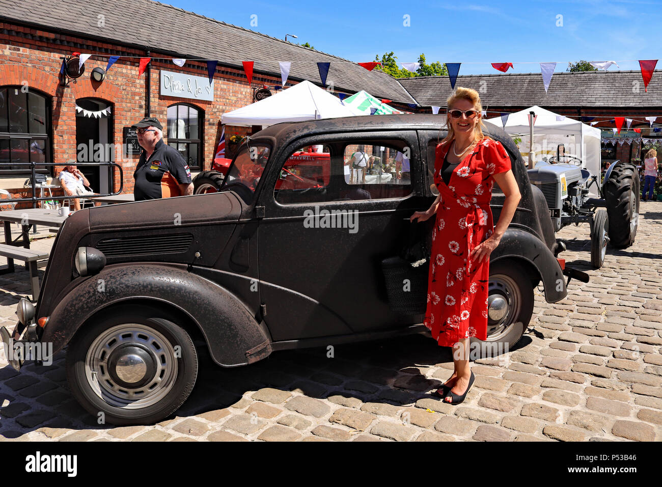 Una signora vestita in stile anni 1940 abito rosso sorge accanto al suo vecchio Ford auto popolari salvato da un garage dove si era fermato per 41 anni. Foto Stock