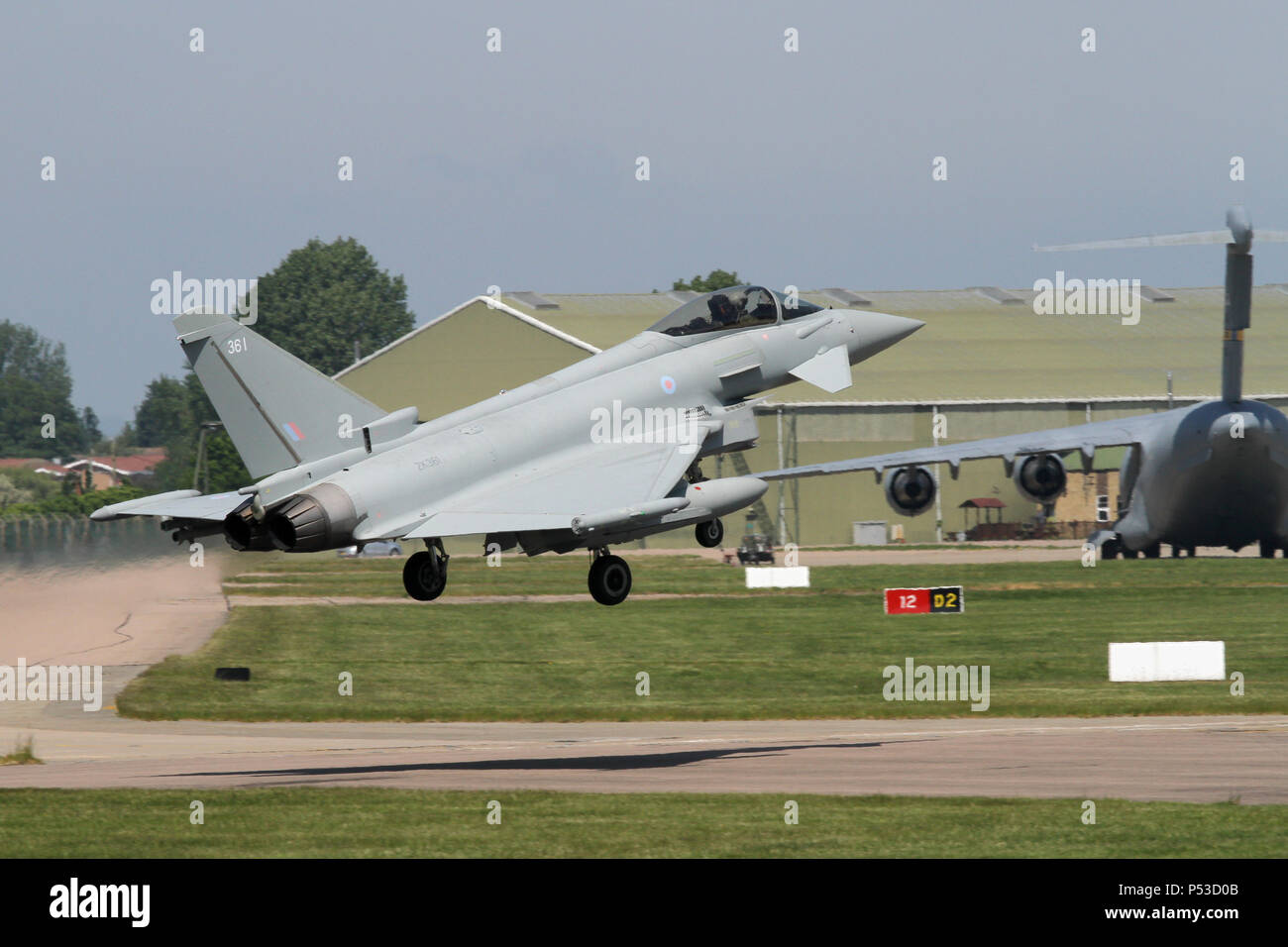 Royal Air Force Typhoon FGR4 sopra la pista e attorno alla terra a RAF Coningsby, casa di base. Nota Il USAF C-17 trasporto parcheggiato dietro. Foto Stock