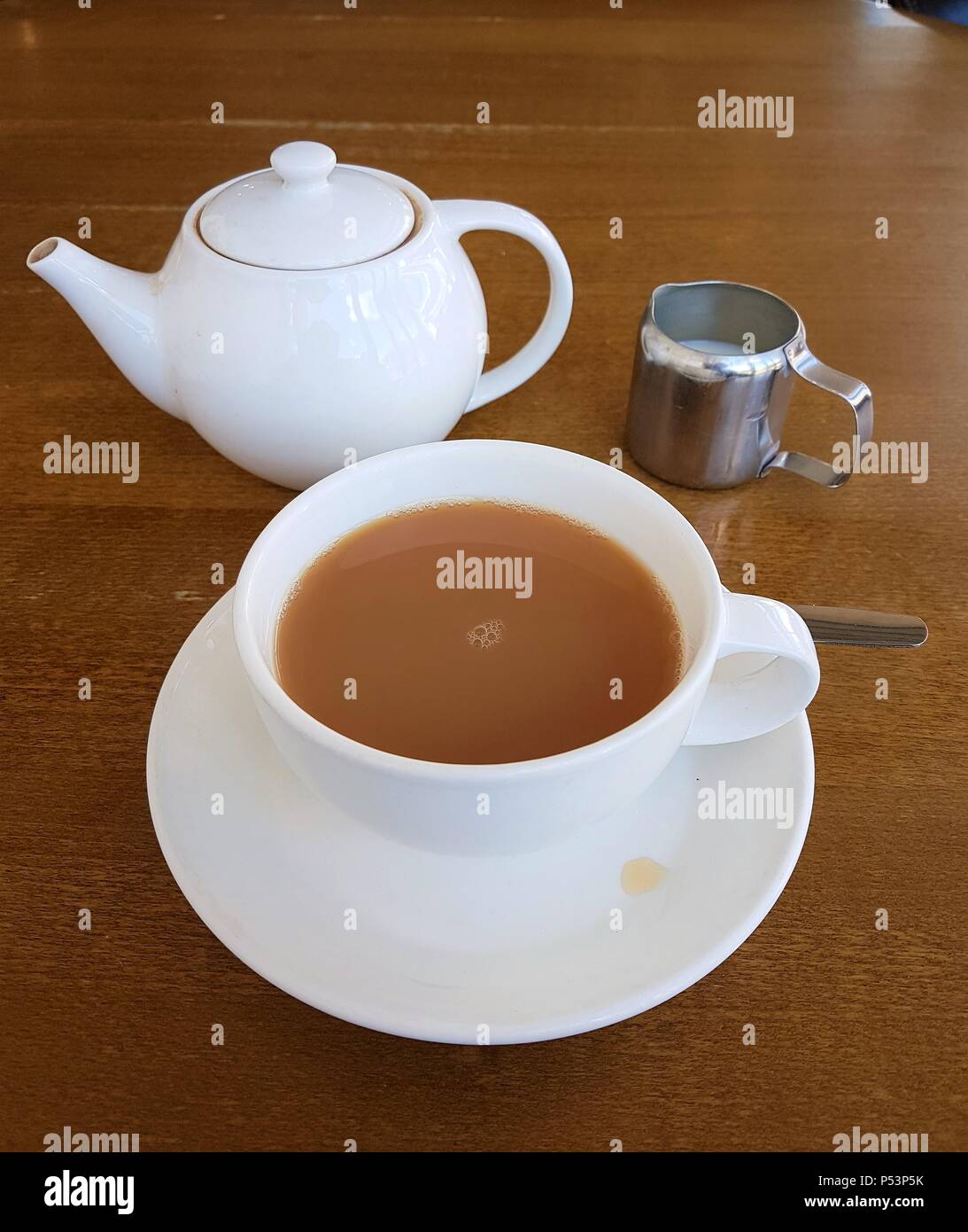 Tazza da tè riempita con tè sul piattino con tè pentola e latte su un tavolo Foto Stock