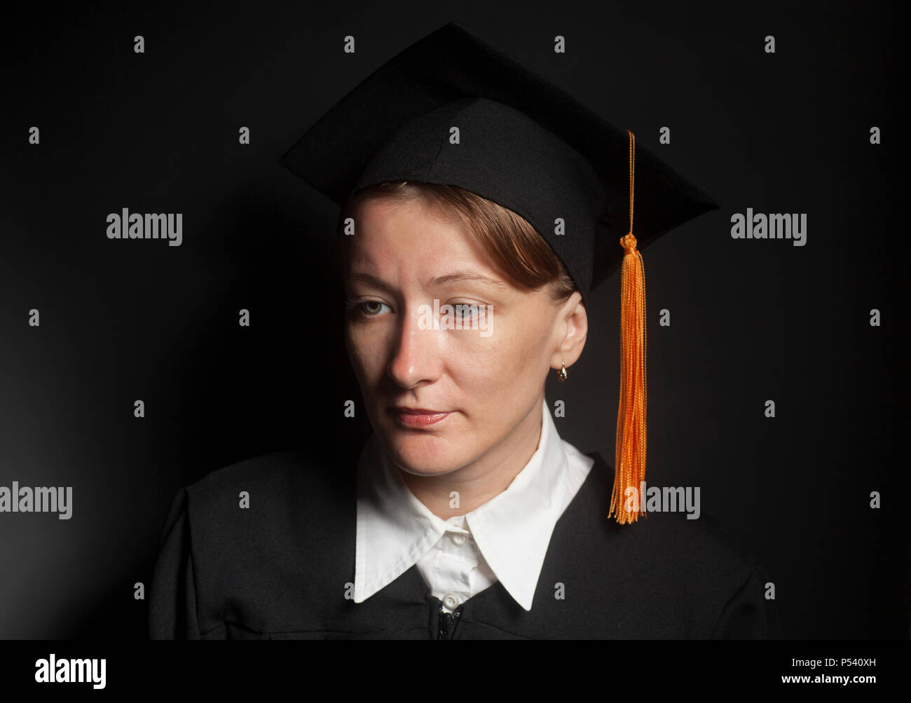 Ritratto di donna bachelor nel mantello nero e il cappuccio di graduazione su sfondo nero Foto Stock