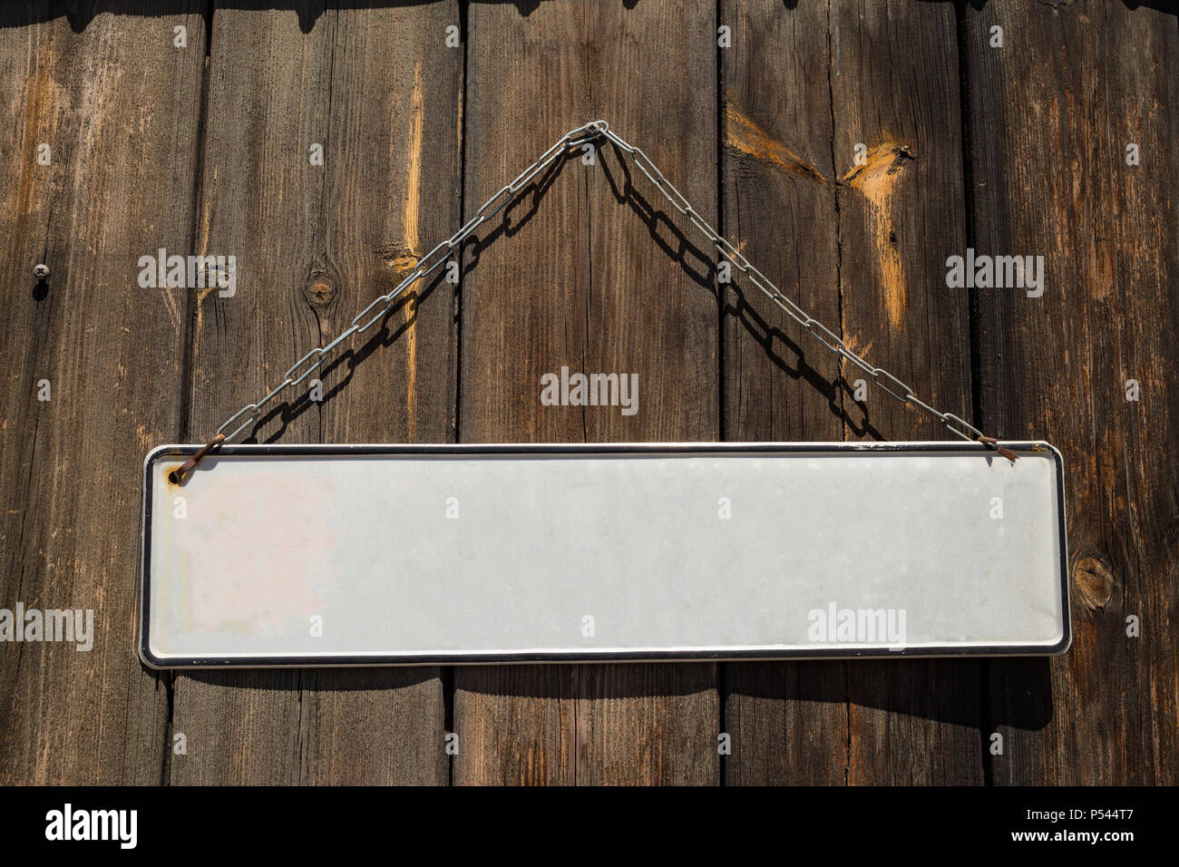 Legno marrone porta con un vuoto bianco etichetta banner appesi da polveri metalliche arrugginite catena nella parte anteriore di essa. Closeup, spazio per il testo. Foto Stock