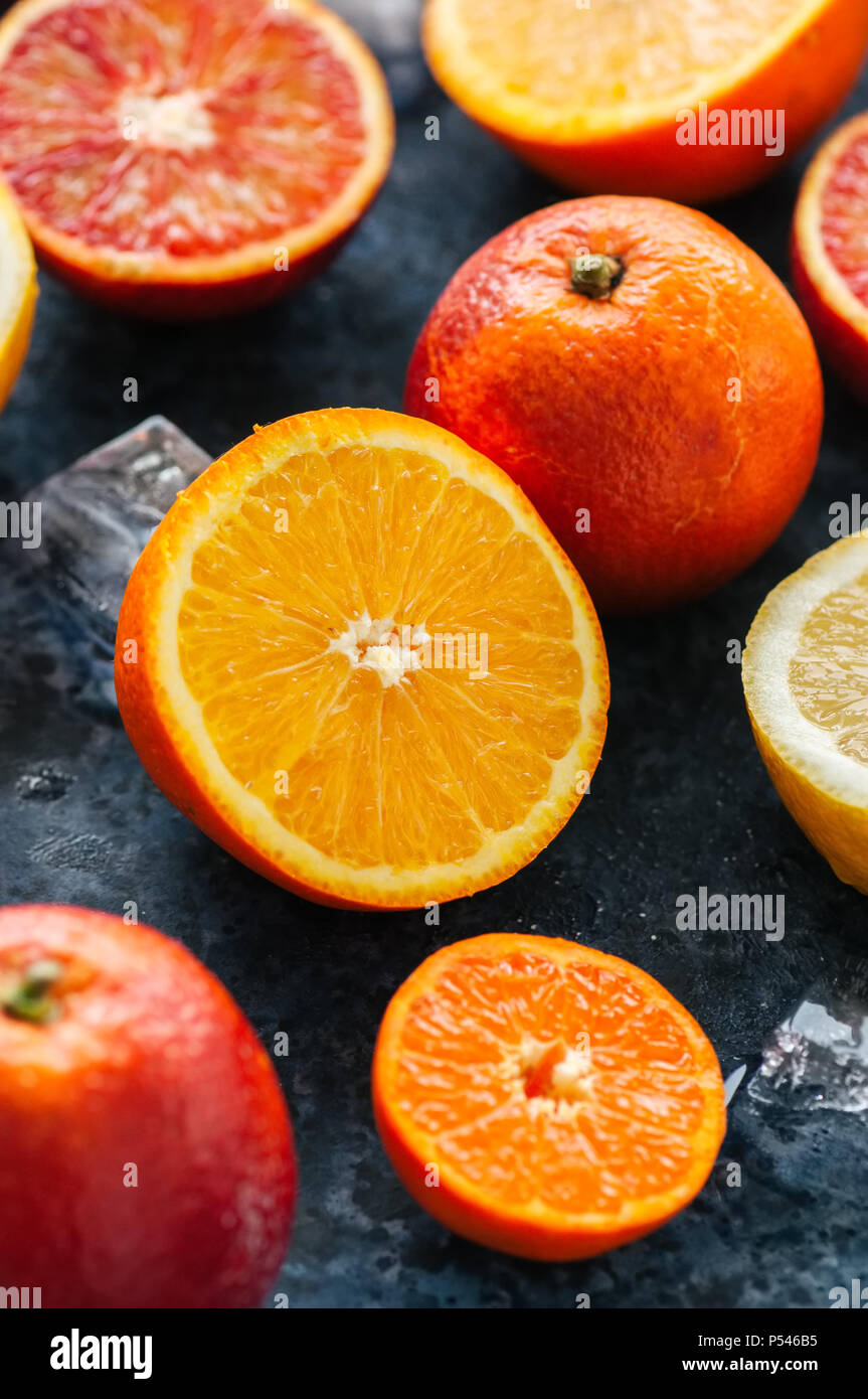 Mix di freschi maturi di agrumi. Il sangue di arance, mandarini, limoni con cubetti di ghiaccio su una pietra blu sullo sfondo. Vista dall'alto. Foto Stock