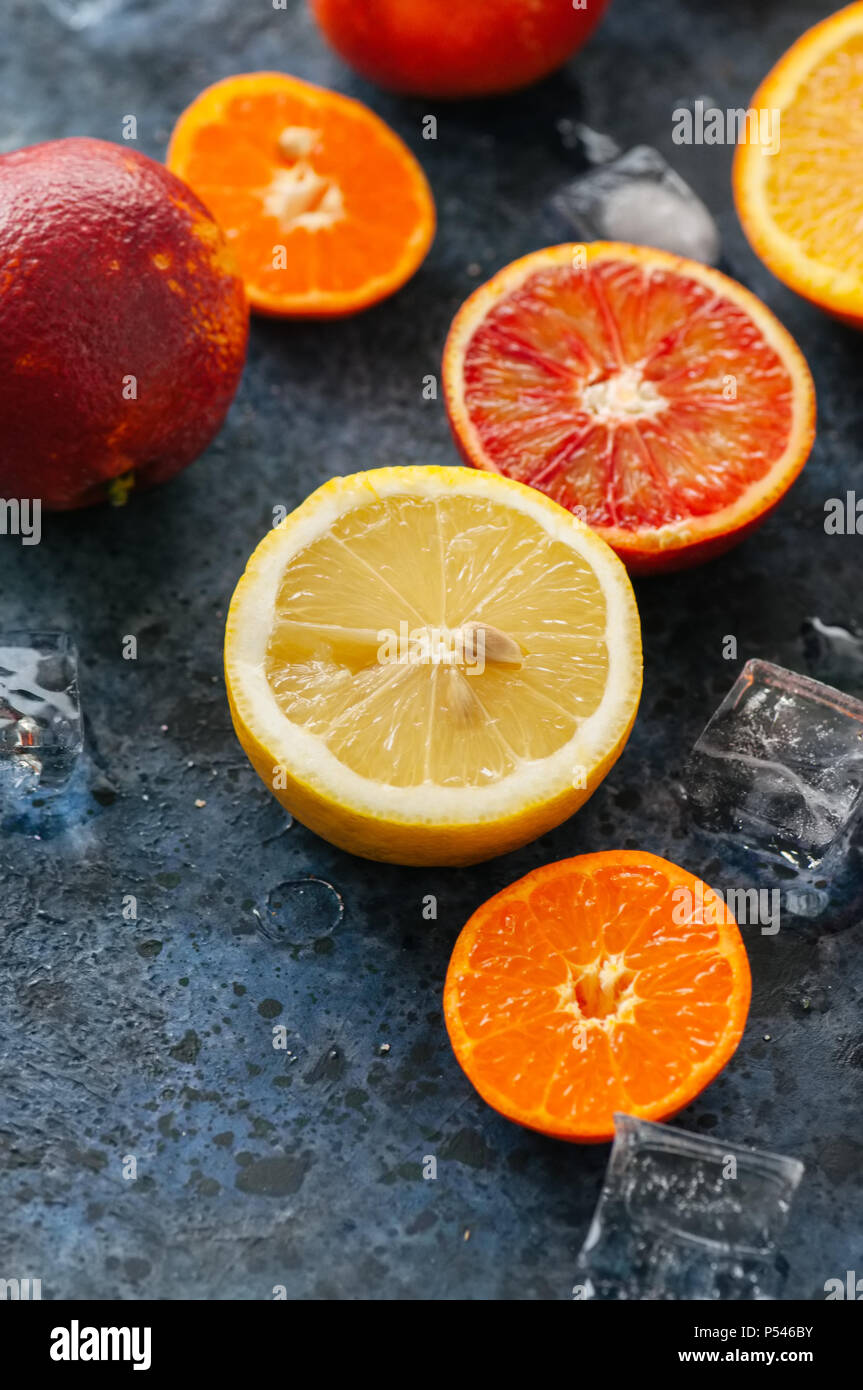 Mix di freschi maturi di agrumi. Il sangue di arance, mandarini, limoni con cubetti di ghiaccio su una pietra blu sullo sfondo. Vista dall'alto. Foto Stock