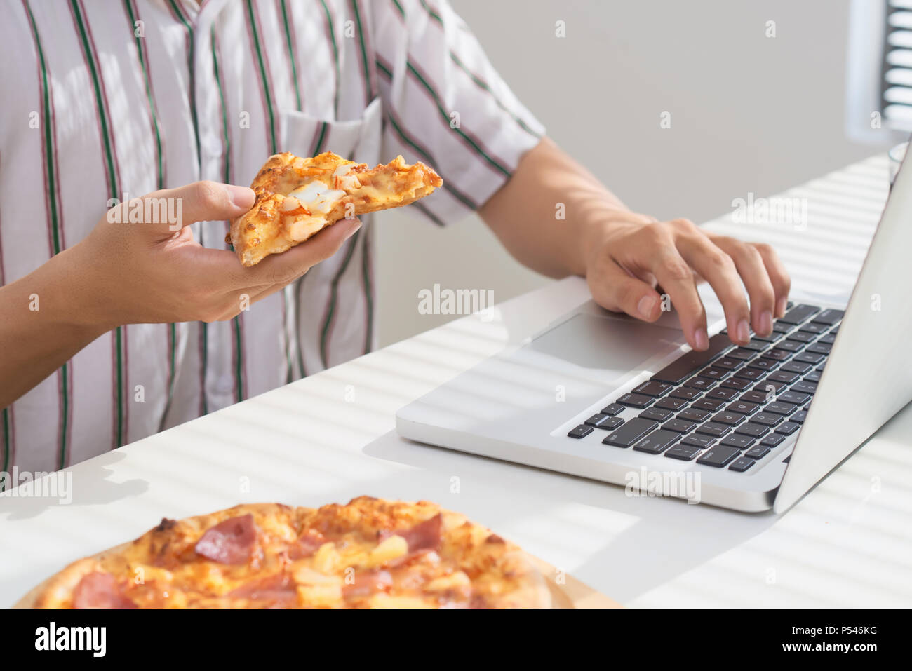 Mangiare la pizza e il social networking con un computer portatile. Foto Stock