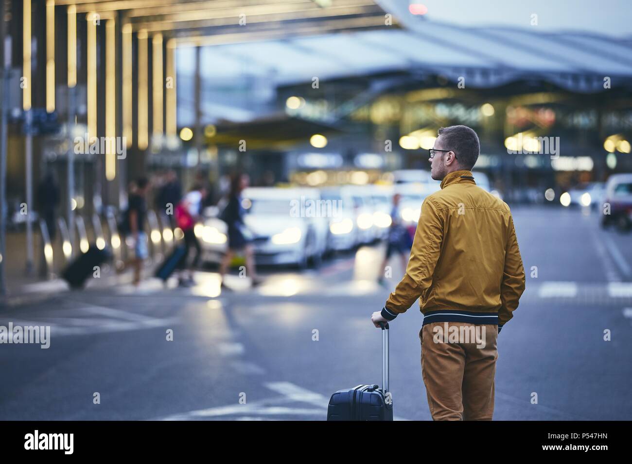 A piedi passeggero al di fuori del terminal dell'aeroporto. Vista posteriore del giovane uomo con i bagagli di notte. Foto Stock